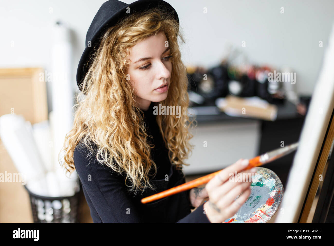 Tattoed Blonde Curly Artist In Black Hat Drawing With Brush And