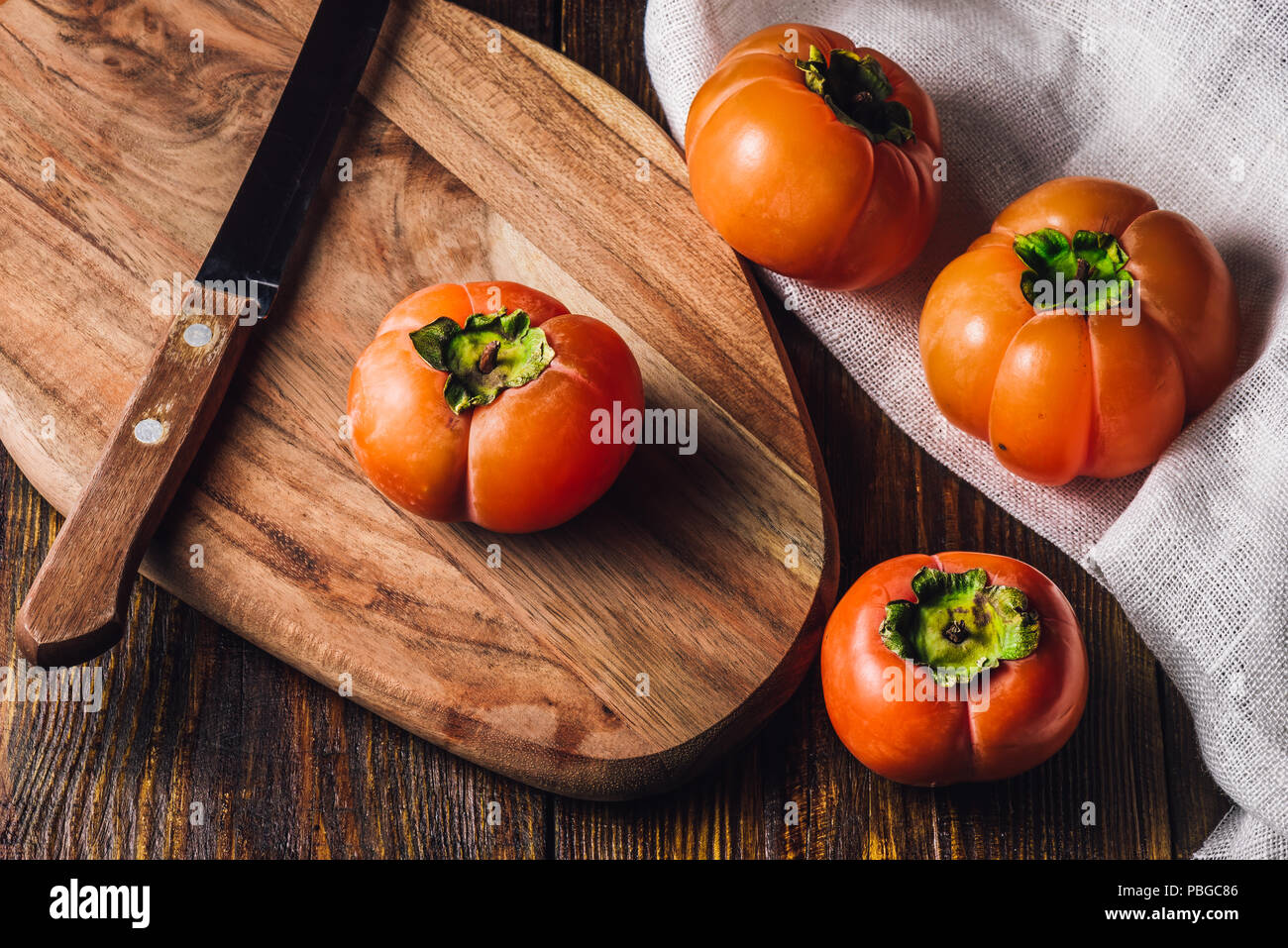 Persimmons with Knife on Wooden Cutting Board Stock Photo