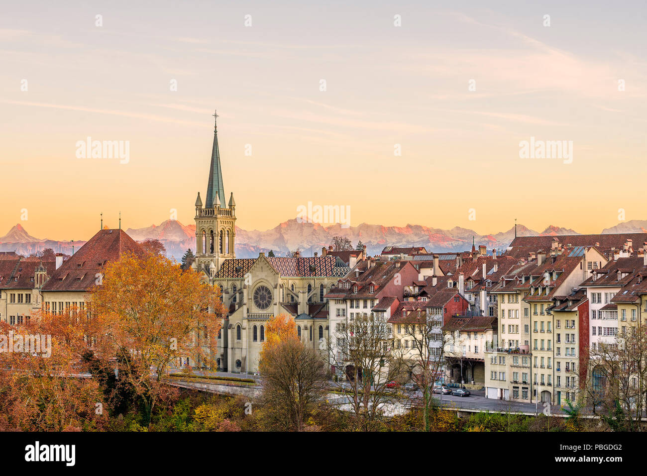 Facades of the old town of Bern, capital of Switzerland, with Swiss alps peaks in the background glowing reddish during an  autumn sunset. Stock Photo