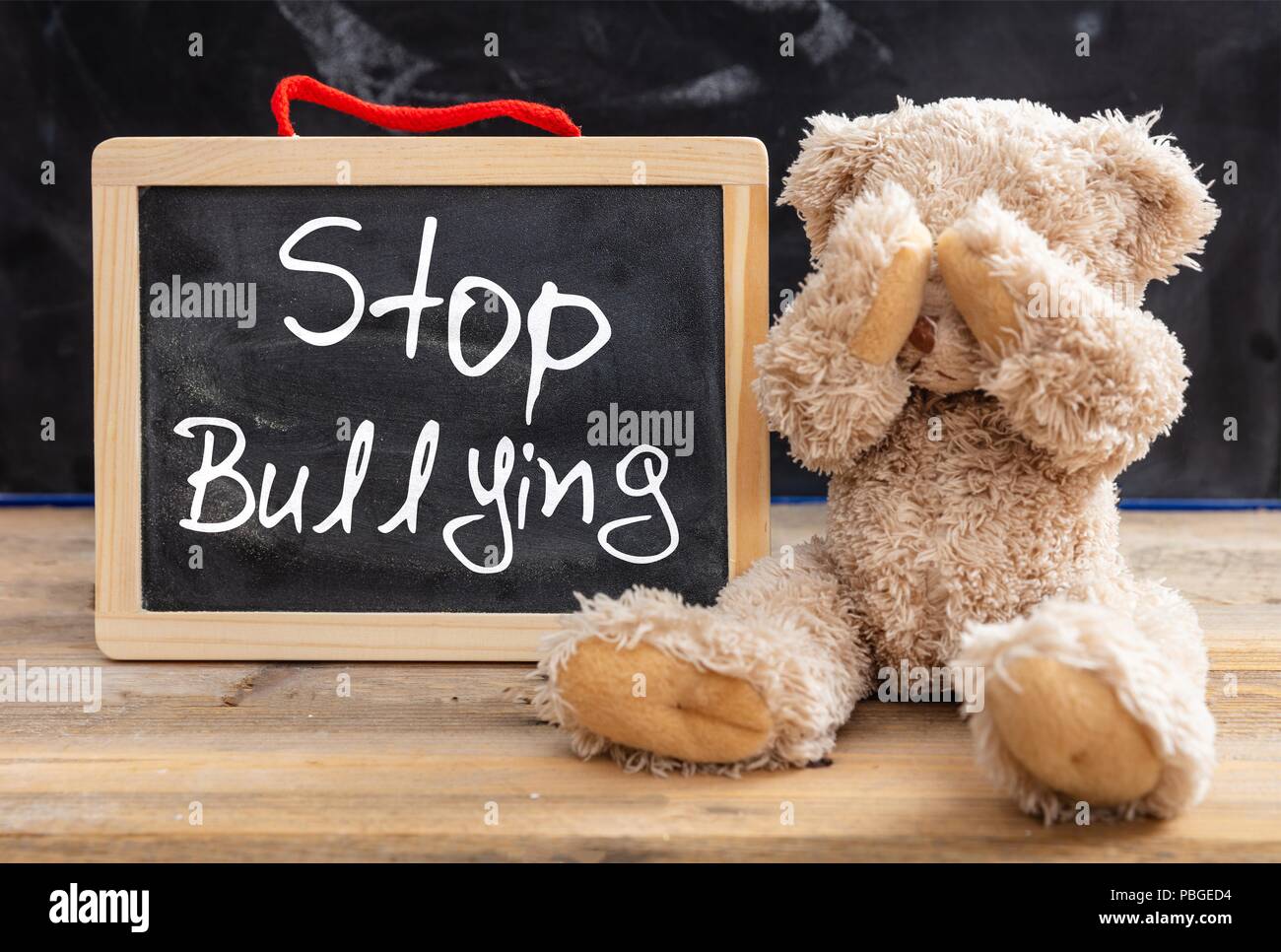 Bullying at school. Teddy bear covering eyes and stop bullying text on a blackboard Stock Photo