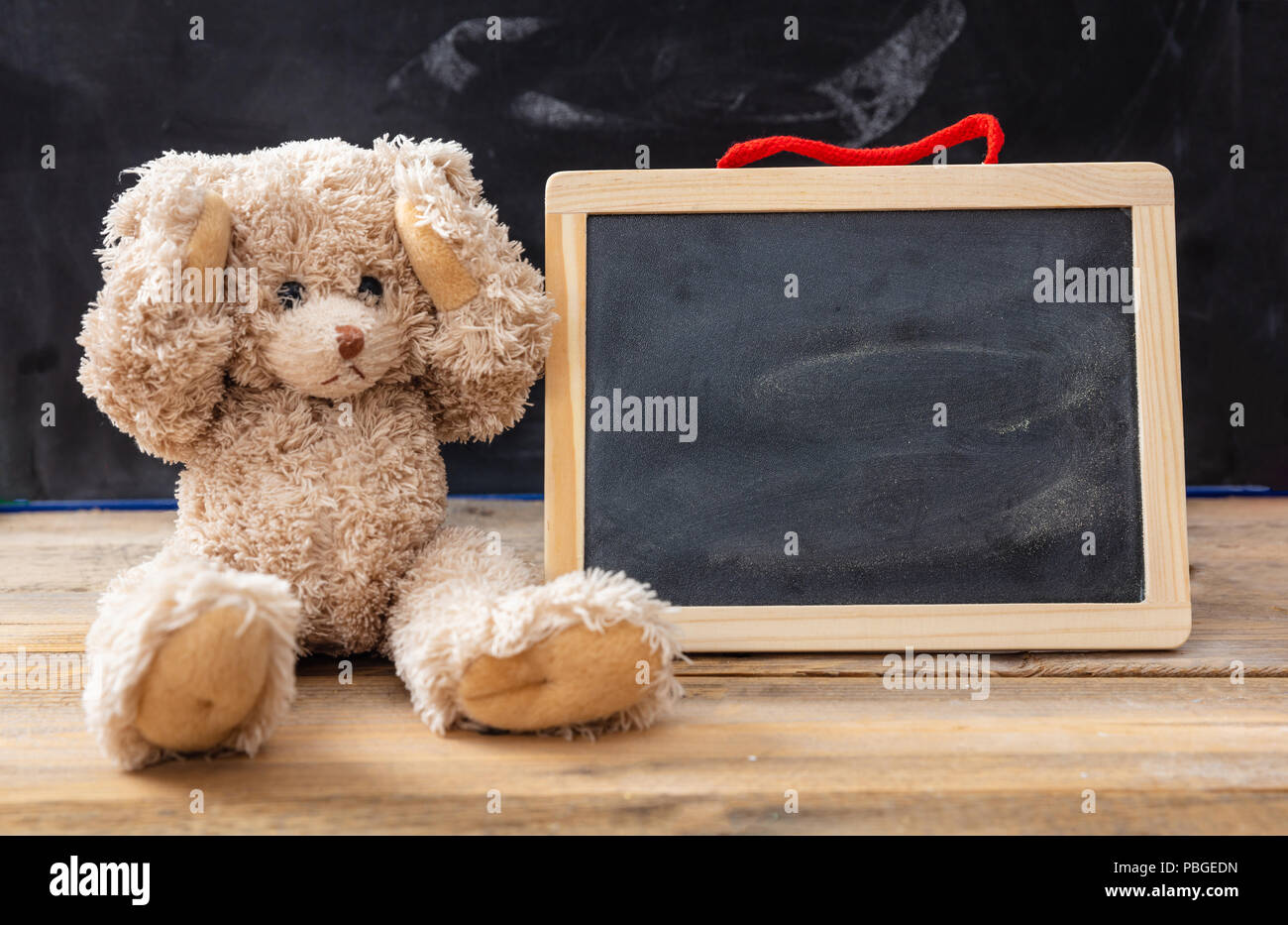 Bullying at school or learning difficulties concept. Teddy bear covering ears and a blank blackboard, space for text Stock Photo