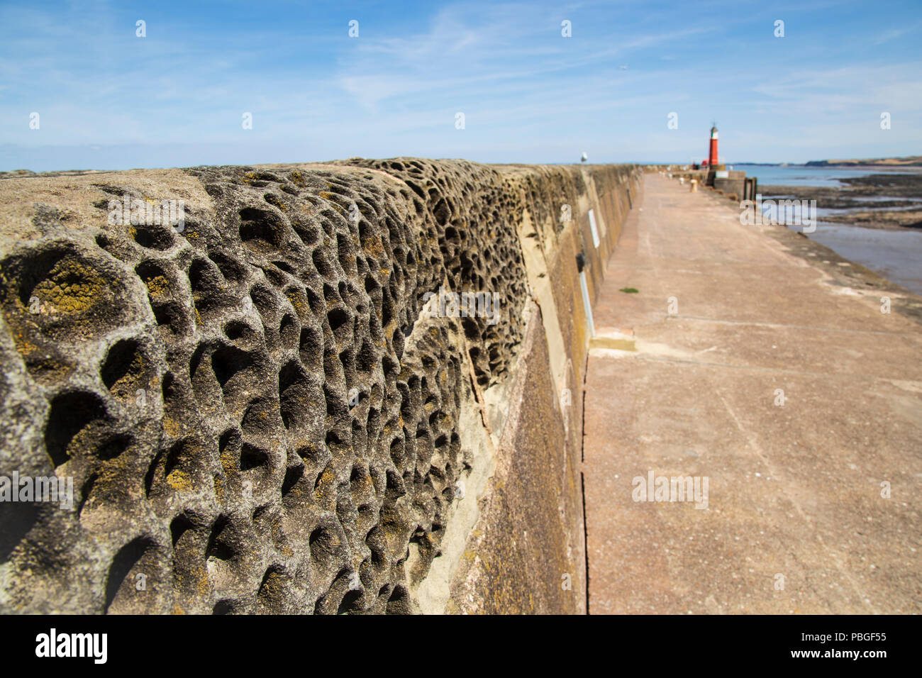 Watchet, Somerset, heavily weathered sea wall near the harbour entrance and the lighthouse. Stock Photo