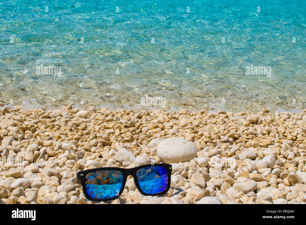 Blue sunglasses on a pebble beach with turquoise sea waters on the ...