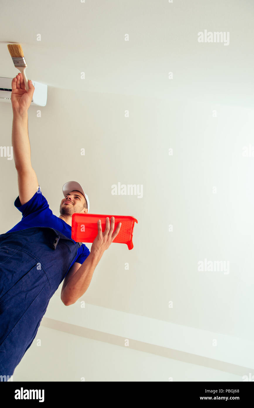 Painter in overall with paintbrush coloring wall in white Stock Photo