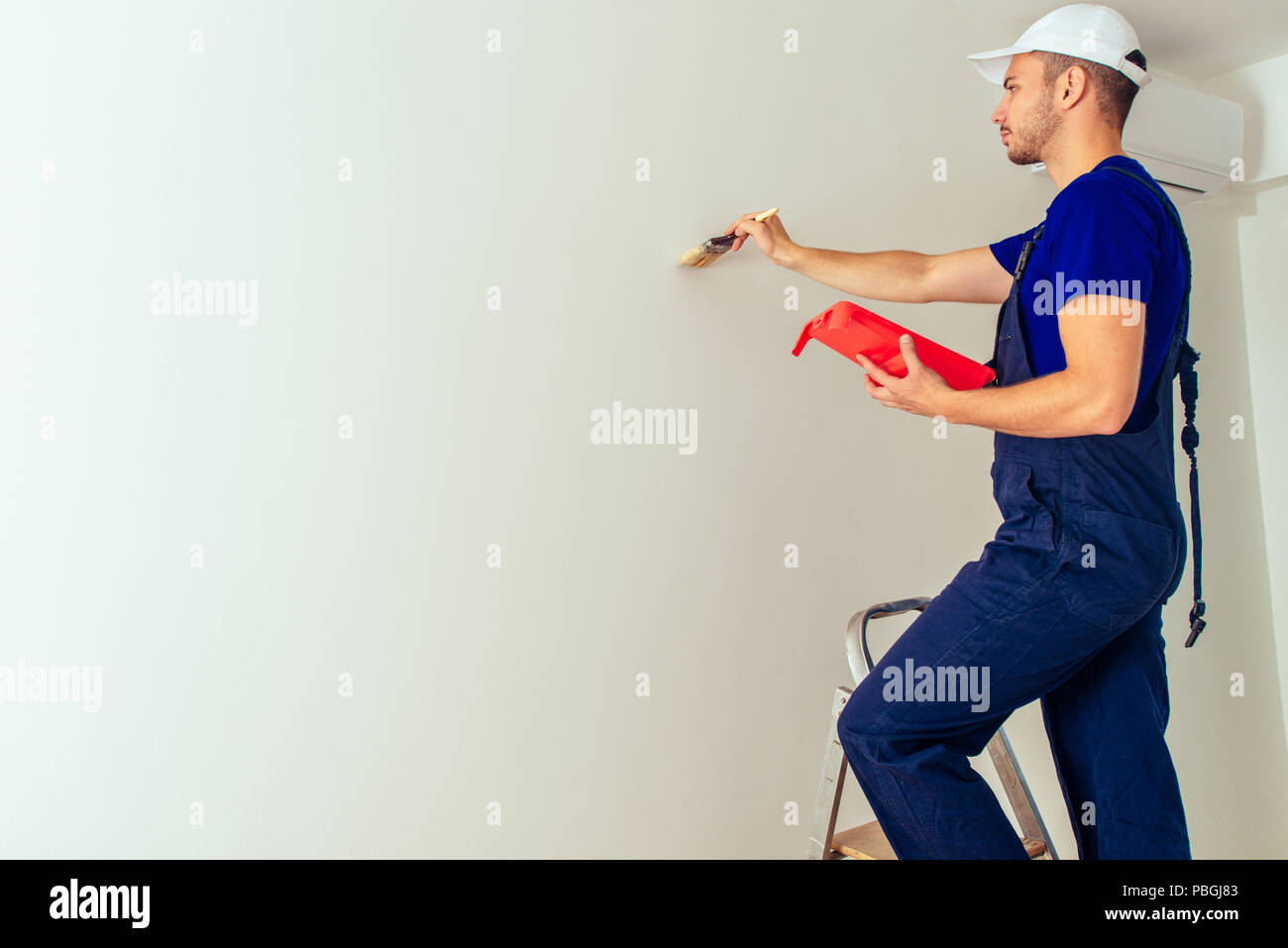 Man with paintbrush in hand standing on a ladder and painting a wall
