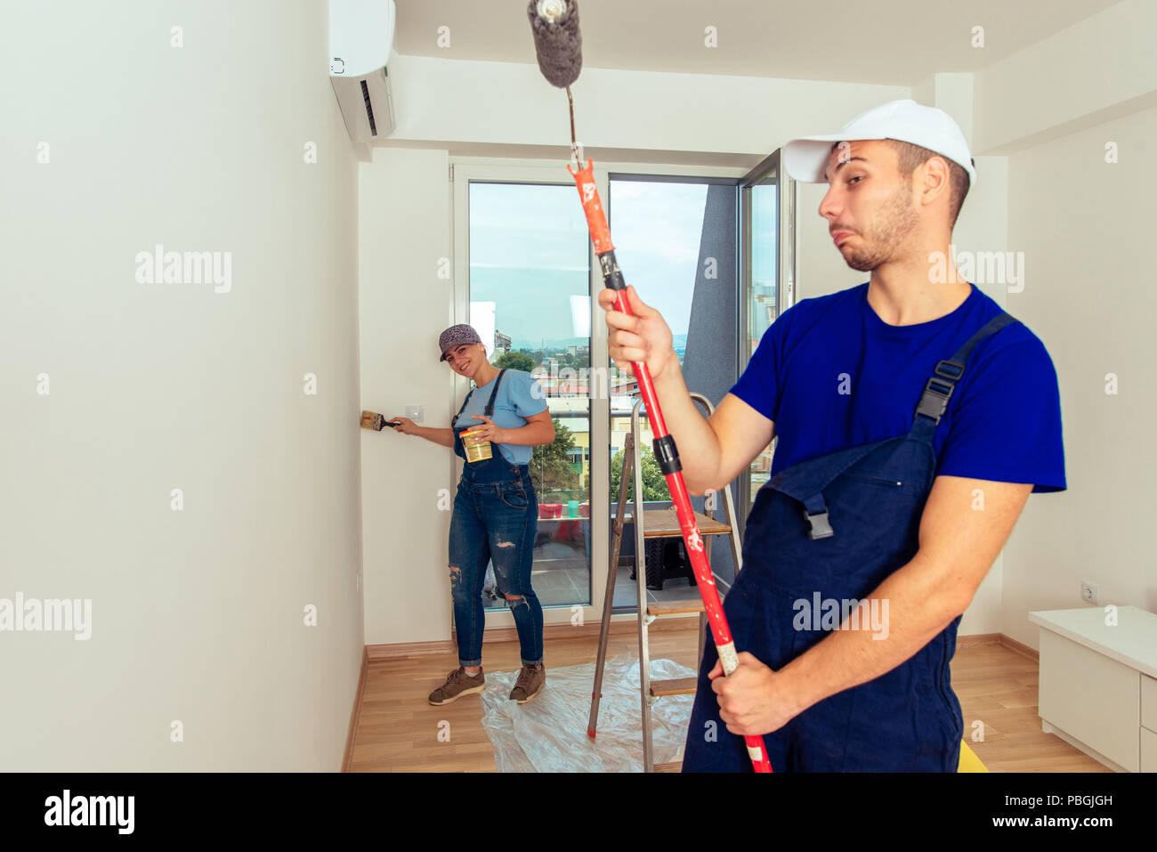 Couple decorating room using paint rollers and paintbrush on wall Stock Photo