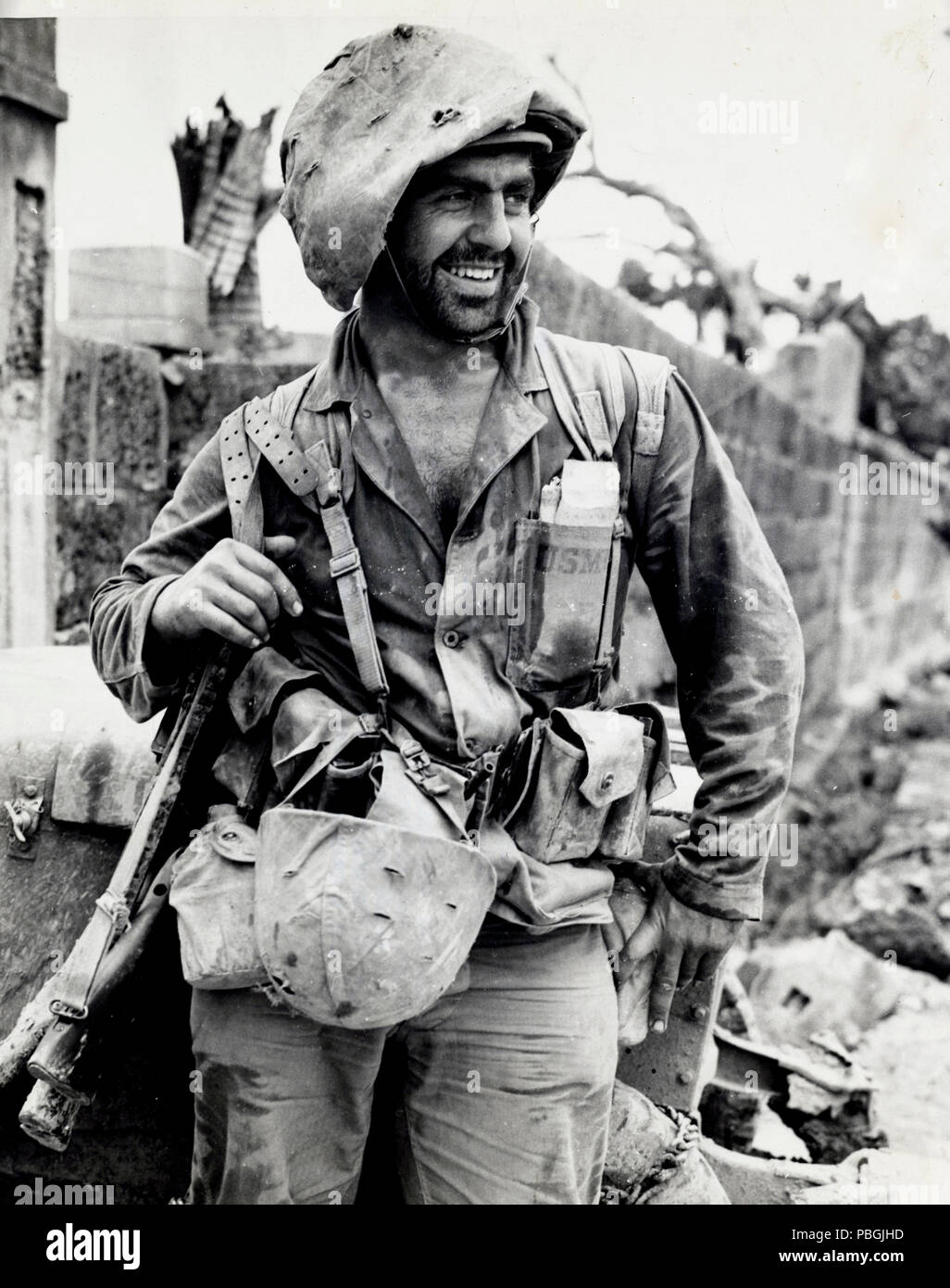 Appearing like a character from a Maudlin cartoon, Marine PFC Harry Kizirian grins after 12 days of battle, but why two rifles and two helmets Stock Photo