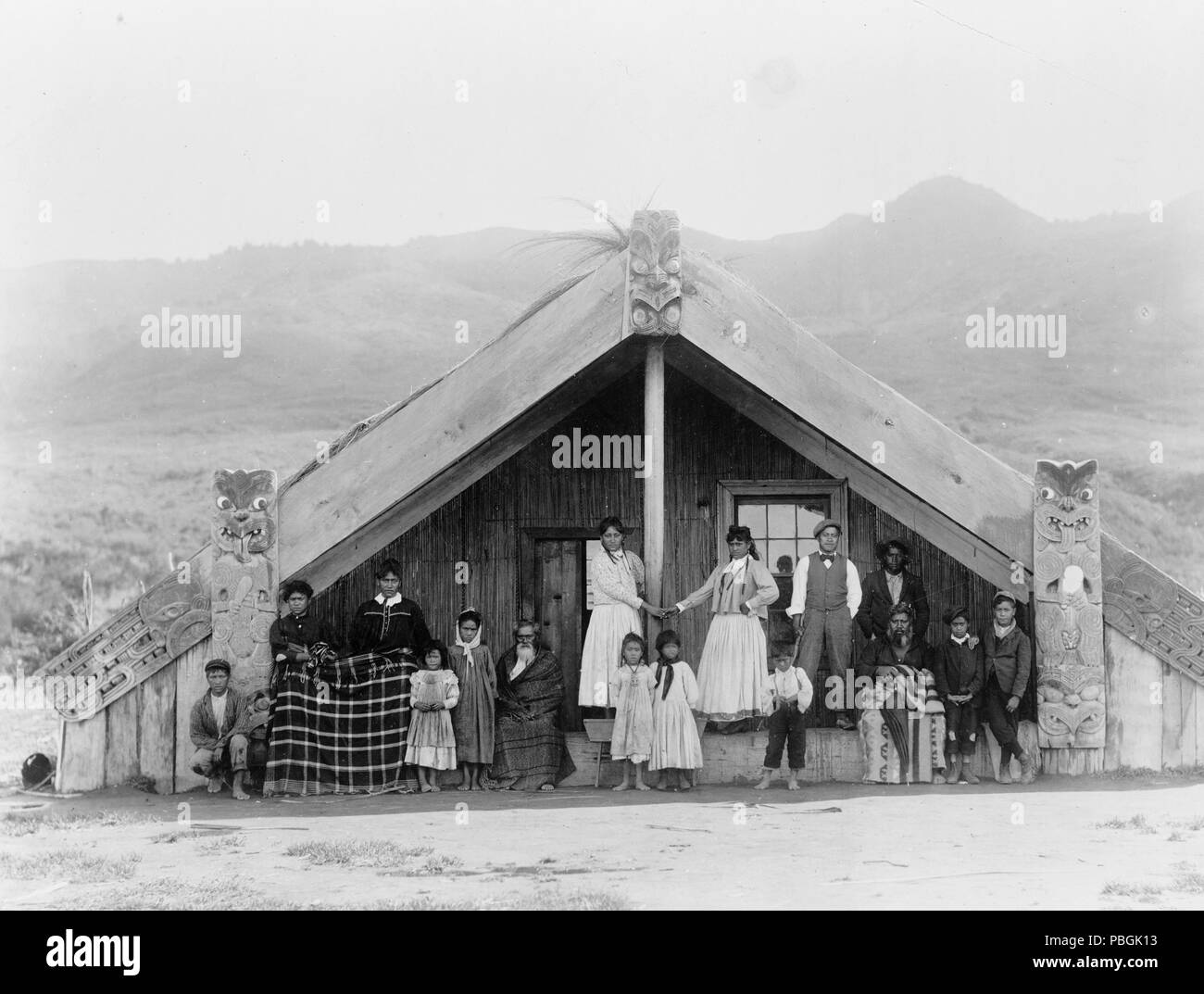 Men, women and children on porch of ceremonial structure with carved wooden sections. (at their talking house) 1880-1920 Maori in New Zealand Stock Photo