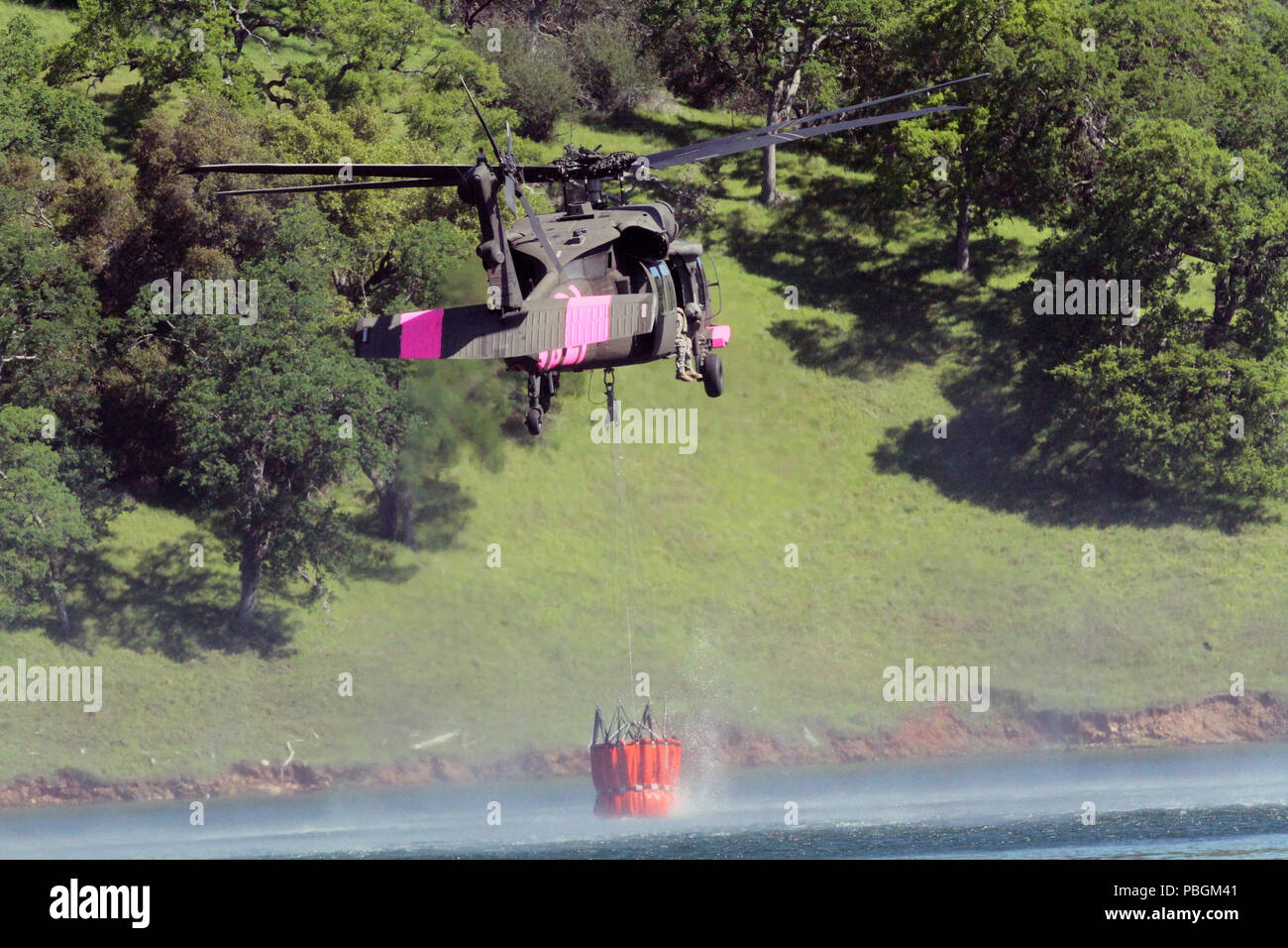 A UH-60 Black Hawk helicopter of the California Army National Guard hovers above Lake Pardee in Ione, California, collecting water in a bucket, April 14, 2018, during wildland firefighting training, a cooperative mission between Cal Guard and the California Department of Forestry and Fire Protection (CAL FIRE). (U.S. Army National Guard photo by Staff Sgt. Eddie Siguenza) Stock Photo