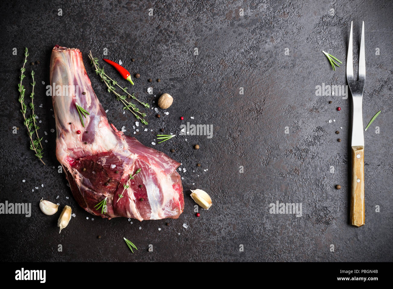 Raw fresh Lamb Meat shank, herbs and fork on black stone background. Stock Photo