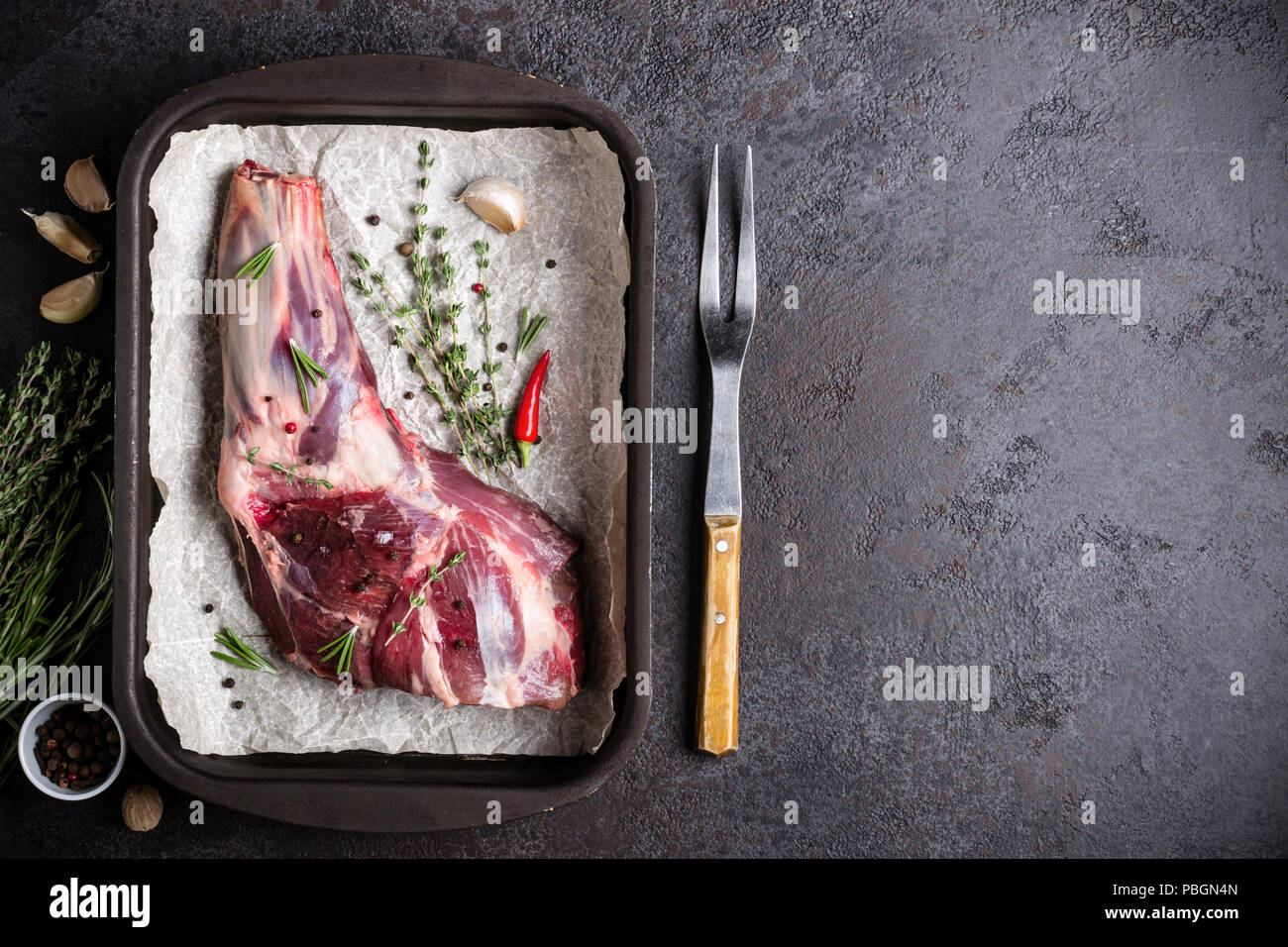 Raw fresh Lamb Meat shank, herbs and fork on black stone background. Stock Photo