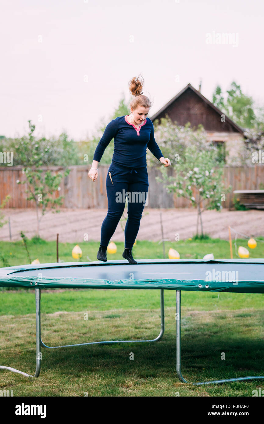 Young White Caucasian Beautiful Plus Size Woman Girl Jumping On Trampoline In Summer Cloudy Day. Stock Photo