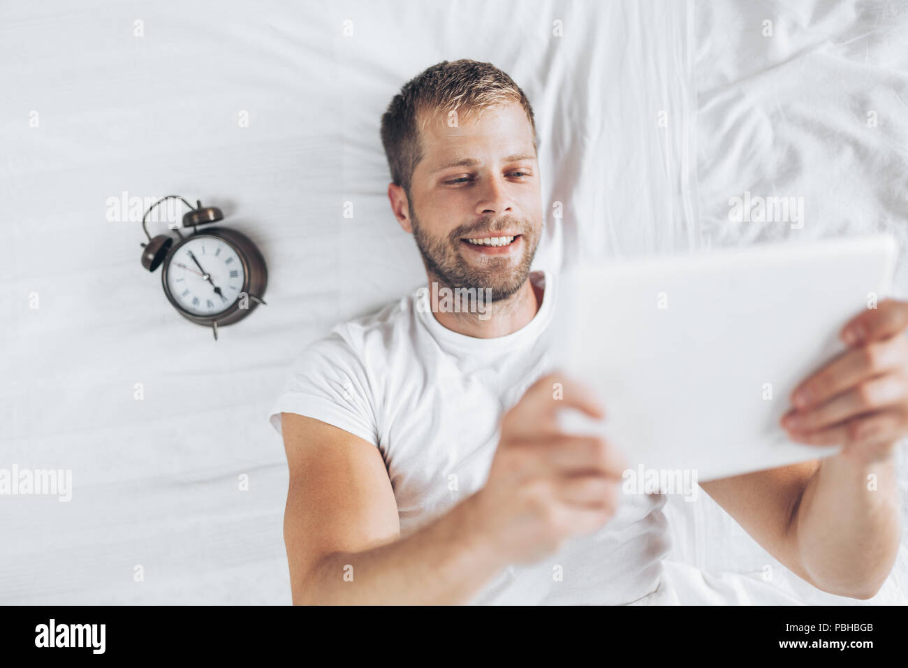 Handsome man using a digital tablet in bed at home Stock Photo