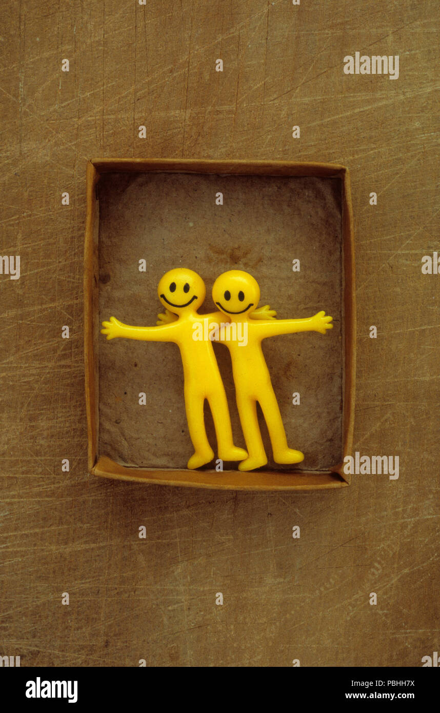 Two yellow plastic smiley bendy men with open arms inside small box Stock Photo