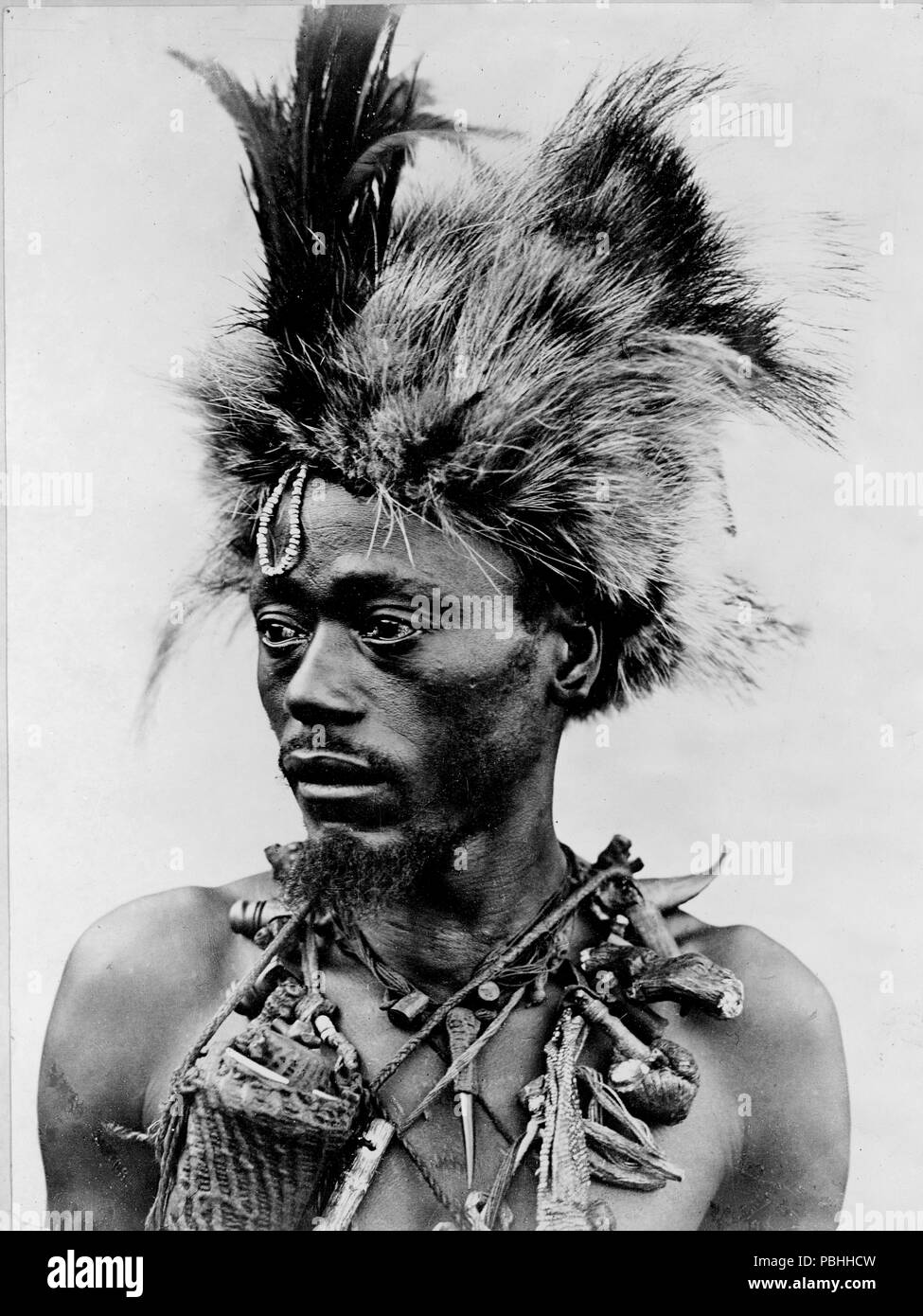 Photo shows a witch doctor, head-and-shoulders portrait, facing left, wearing headdress and many necklaces. 1920-1930 Stock Photo
