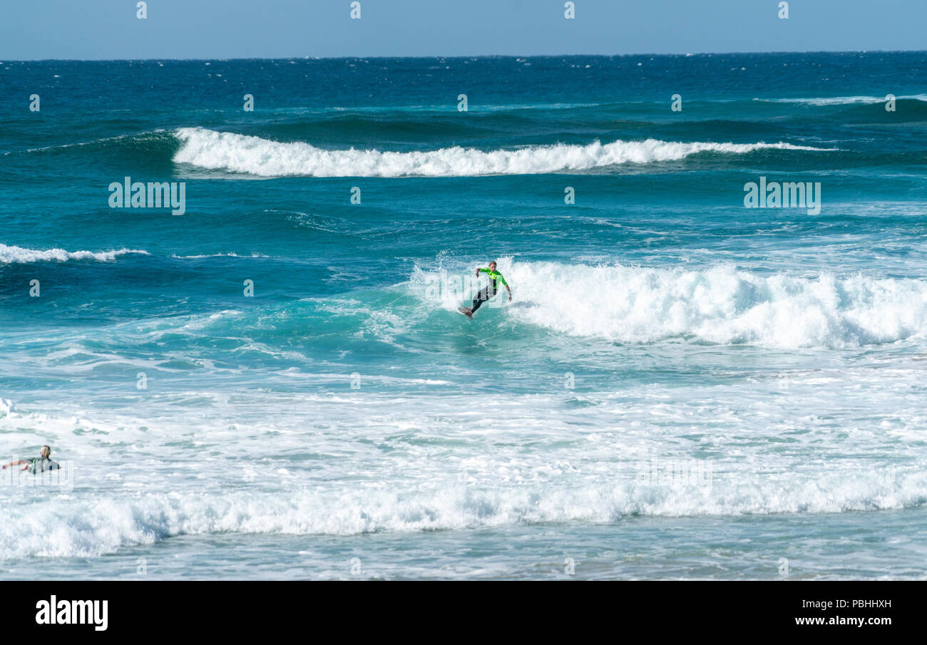 COOLANGATTA, AUSTRALIA - JULY10 2018; Wide surf beach with surfer riding through white wave foam with deep turquoise sea behind Stock Photo