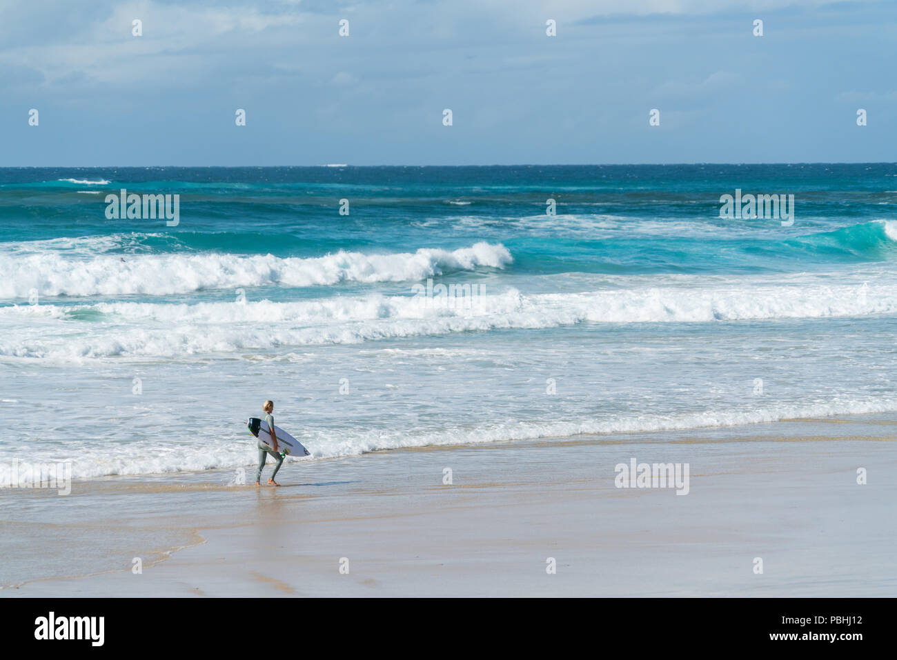 COOLANGATTA, AUSTRALIA - JULY10 2018; Wide surf beach with surfer carrying surfboard along beach in front of surf Stock Photo