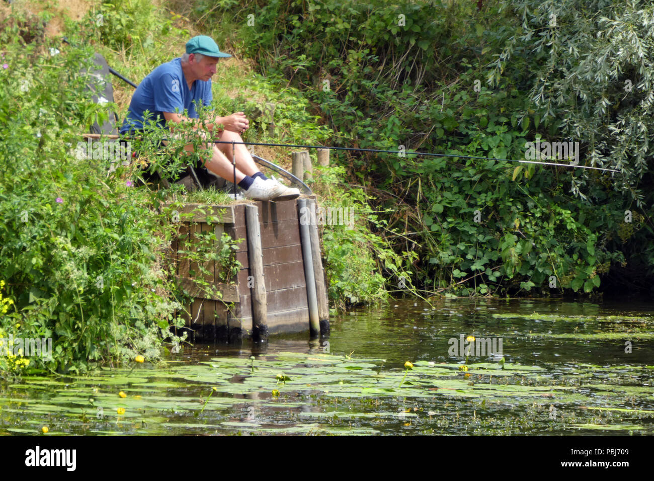 Man sitting by river bank fishing, river Medway, Kent, England
