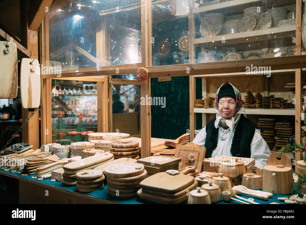 Tallinn, Estonia - December 21, 2017: Old Woman Seller Sells Various Natural Wooden Crafts At Winter Christmas Market. Popular Souvenir From Baltic Co Stock Photo