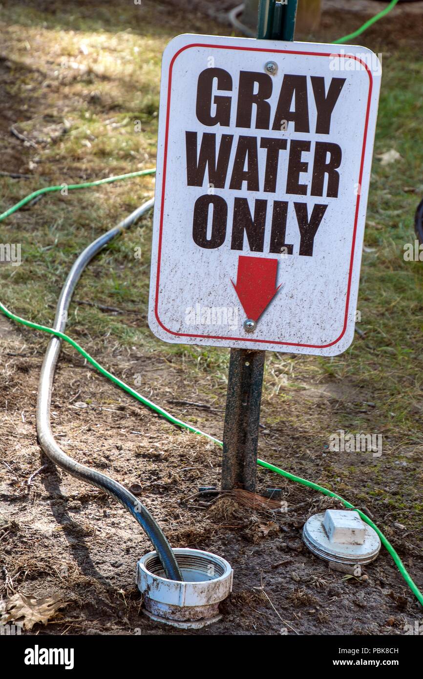 gray water warning sign on metal post in dirt with dirty hoses Stock Photo
