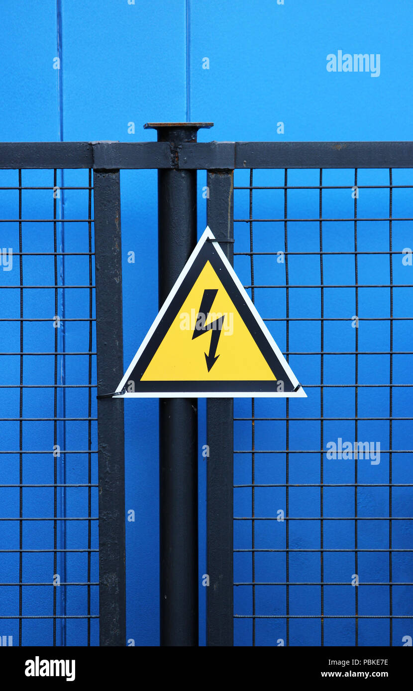 High voltage triangle warning sign mounted on a metal lattice fence on ...