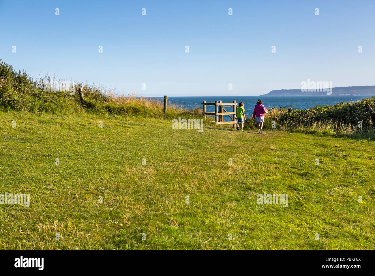 Two young children walking through a wooden gate on a public footpath near Osmington Mills, Weymouth, England, UK Stock Photo