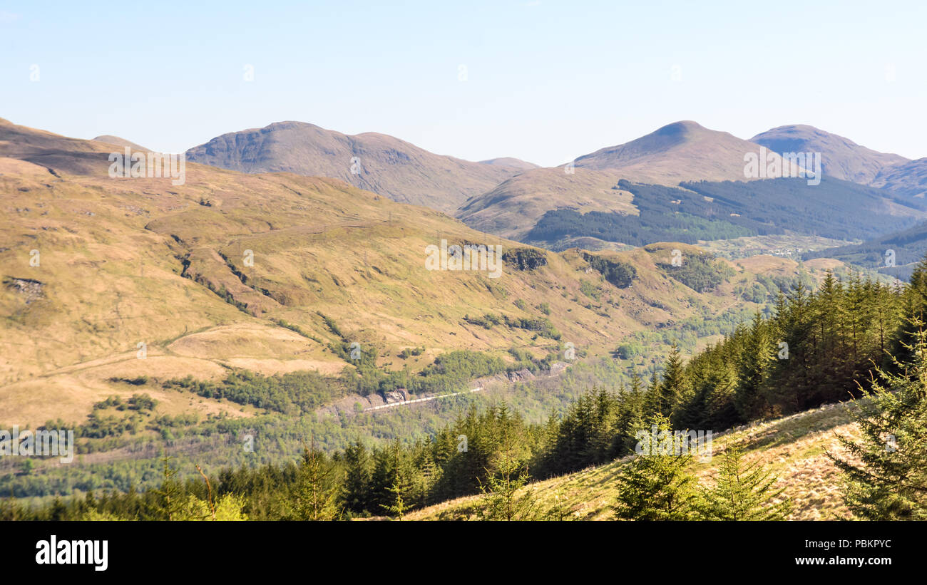 A freight train passes Arrochar on the West Highland Line railway, as seen from the slopes of Ben Arthur mountain. Stock Photo