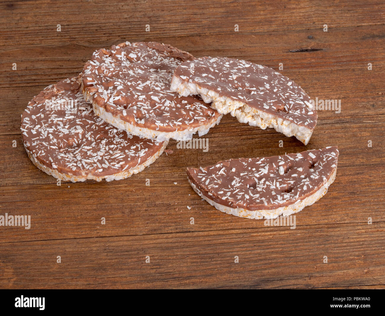 Rice cakes, crackers with milk chocolate and coconut on naturalwood board. Healthy crunchy treat. Stock Photo