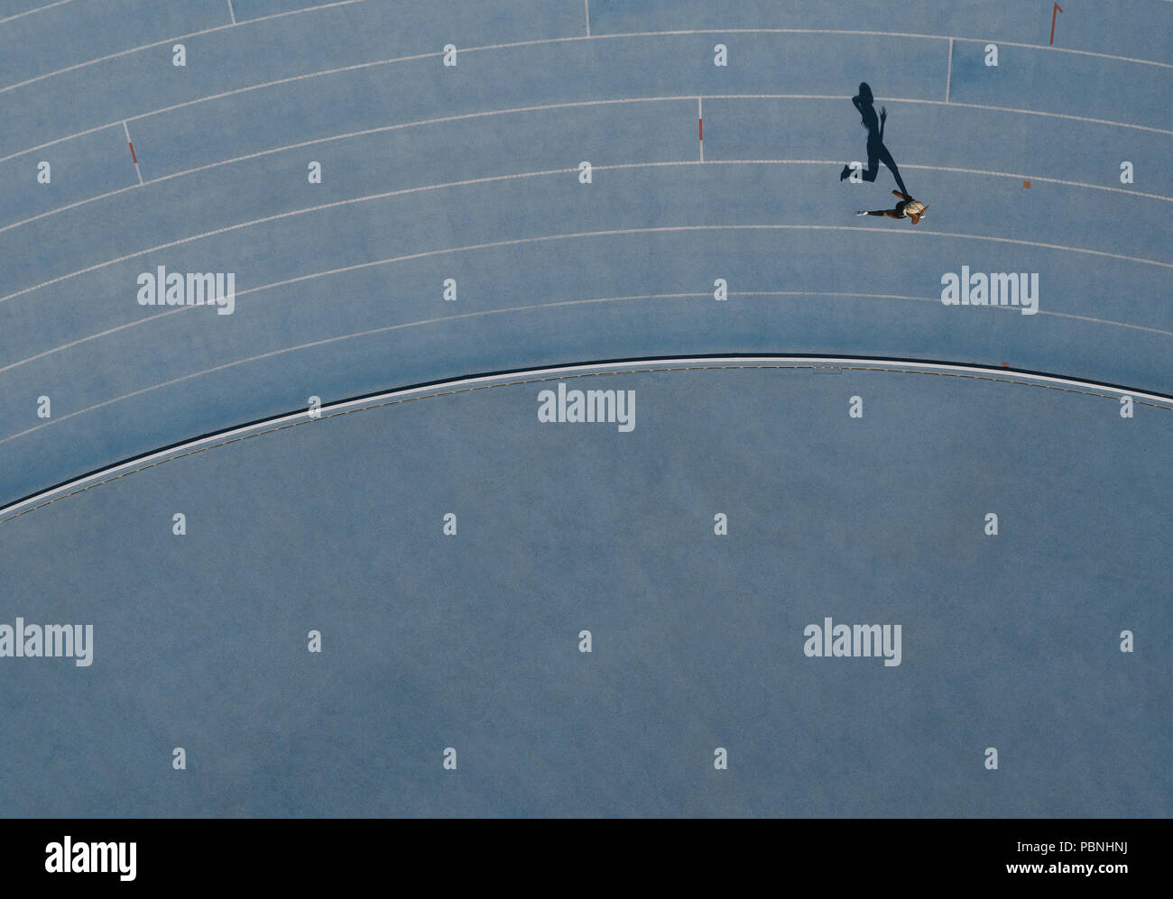 Sprinter running on athletic track. Top view of a sprinter running on race track in a stadium with shadow falling on the side. Stock Photo