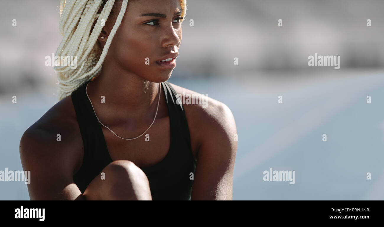 Female athlete sitting on the running track and relaxing after the sprint. Close up of woman athlete sitting inside a track and field stadium looking Stock Photo