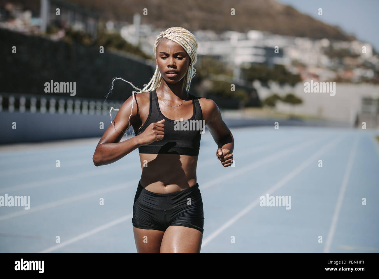 Female athlete sprinting on a running track in a stadium. Female runner practicing her sprint on an all-weather running track. Stock Photo