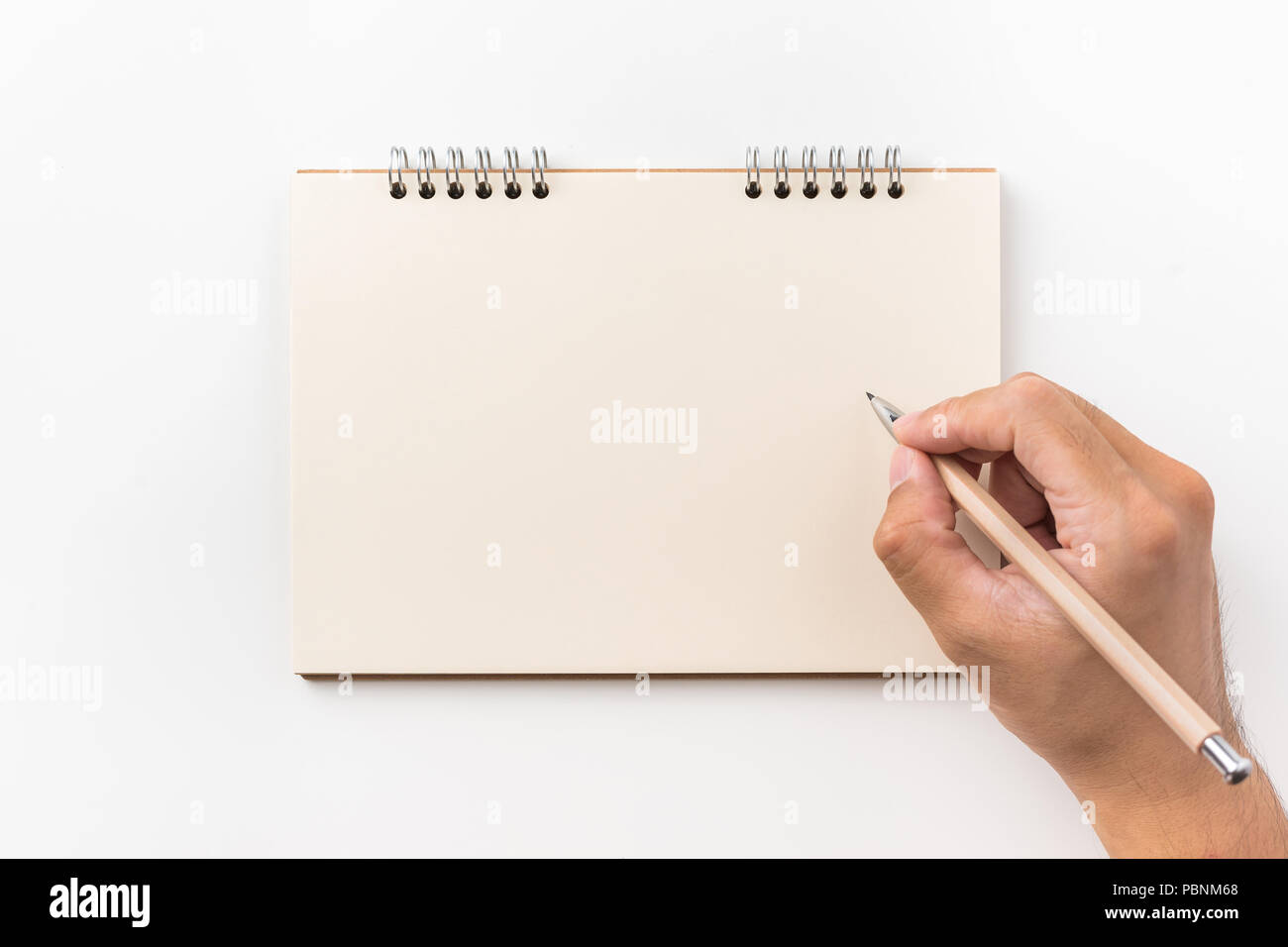 Design concept - Top view of kraft spiral notebook, blank page and man's hand holding wood pen isolated on white background for mockup Stock Photo