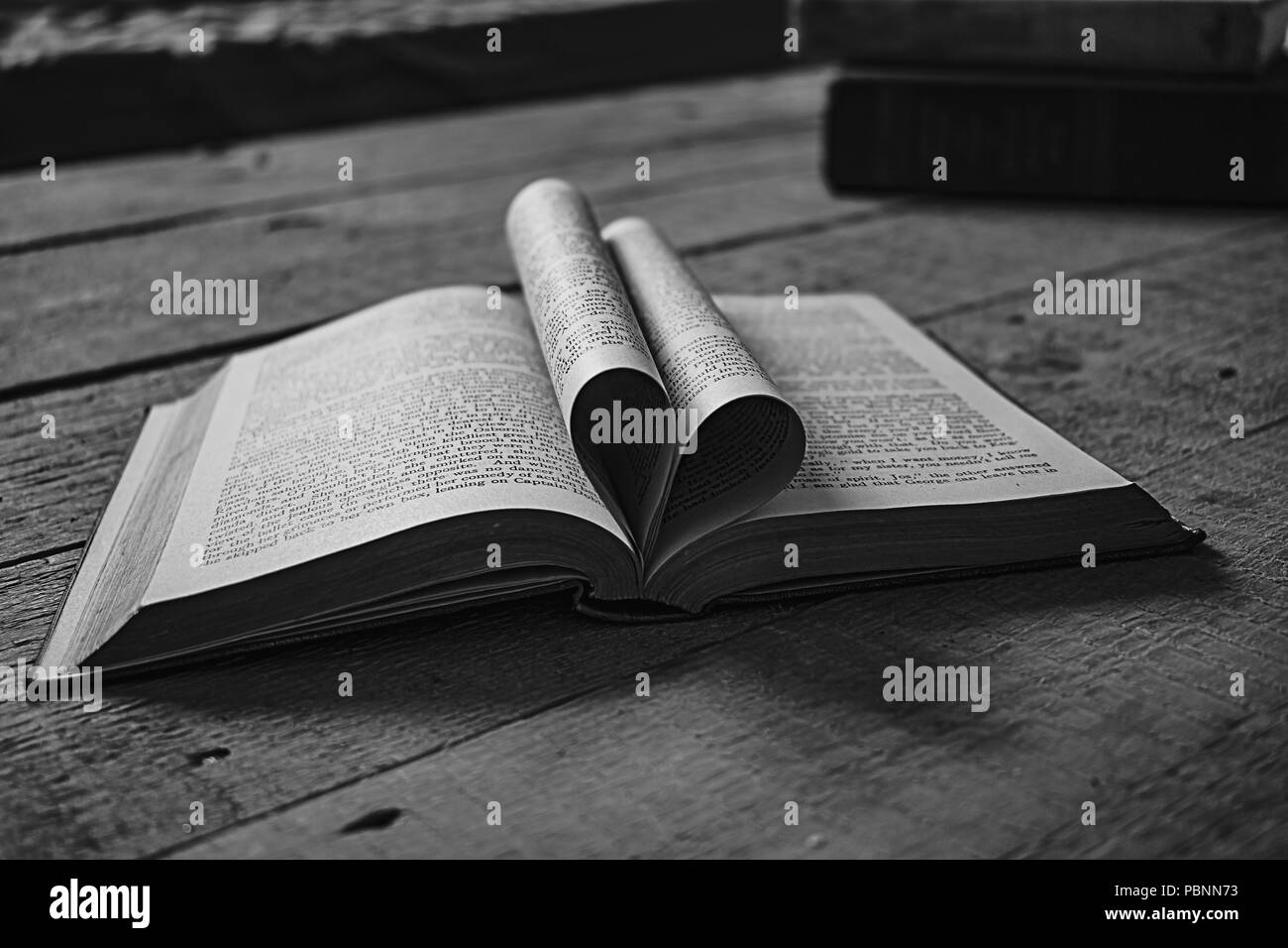 Old book, heartshaped pages open in the middle on a wooden table, perfect for inspirational or magical quotes. Stock Photo