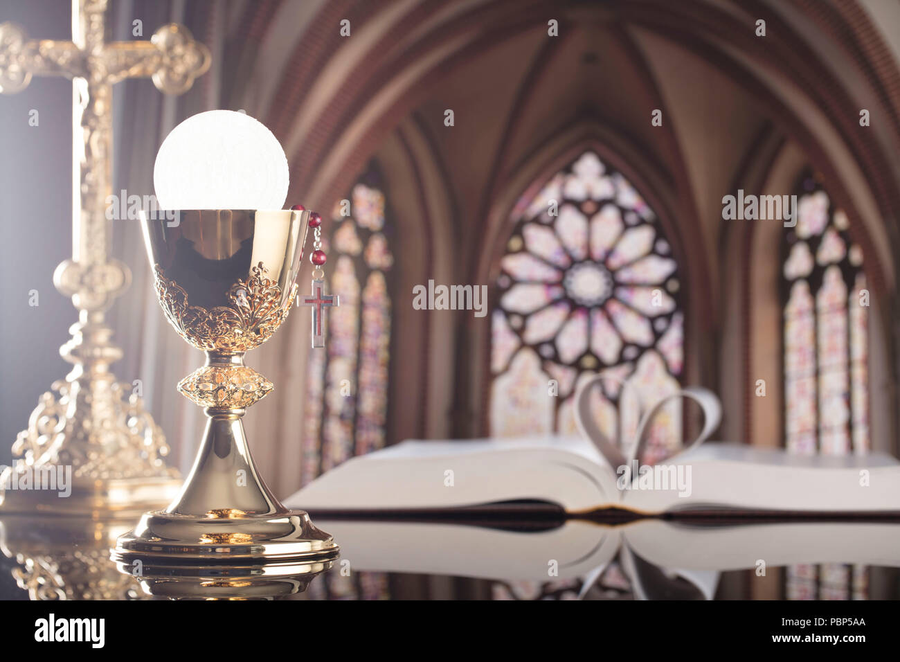 Roman Catholic Church theme. The Cross, Holy Bible, rosary and golden chalice on the altar. Stock Photo
