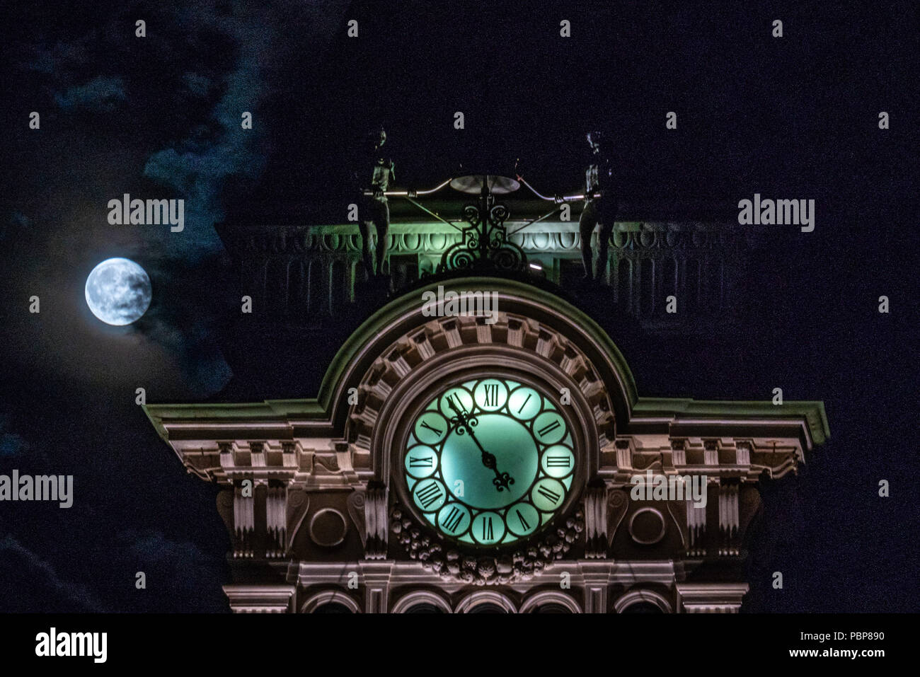 Trieste, Italy, 28 July 2018.  The full moon appears from the clouds behind the top of Trieste's City Hall in Piazza Unità d'Italia. The figures that  Stock Photo