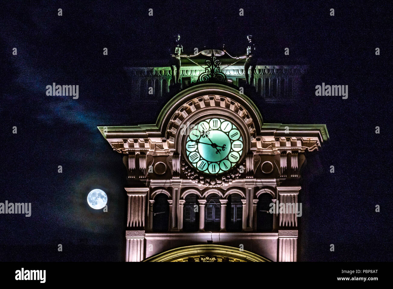 Trieste, Italy, 28 July 2018.  The full moon appears from the clouds behind the top of Trieste's City Hall in Piazza Unità d'Italia. The figures that  Stock Photo