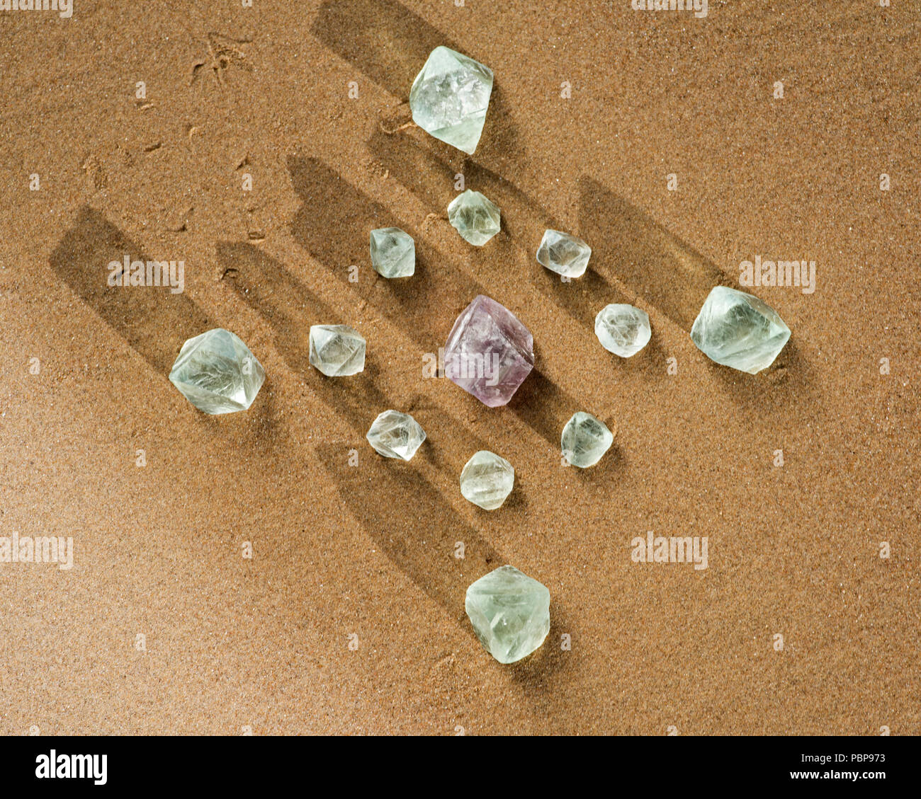 Crystal grid with Purple and Green Fluorite Natural Octahedron Crystals on the beach at sunrise. Stock Photo