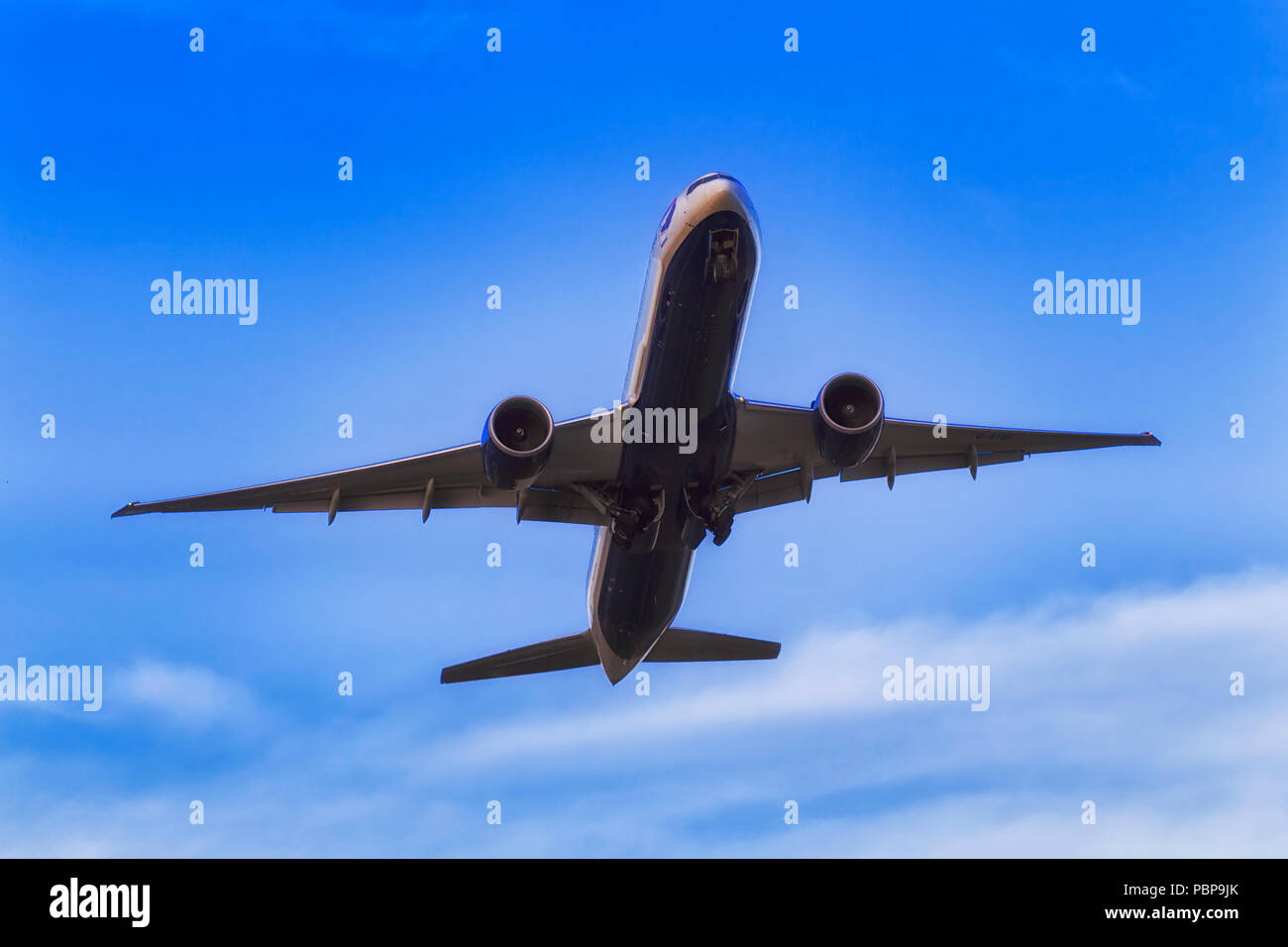 Underbelly of taking off modern jet airplain in blue sky over Sydney International airport with chassis still off and two engines under wings. Stock Photo
