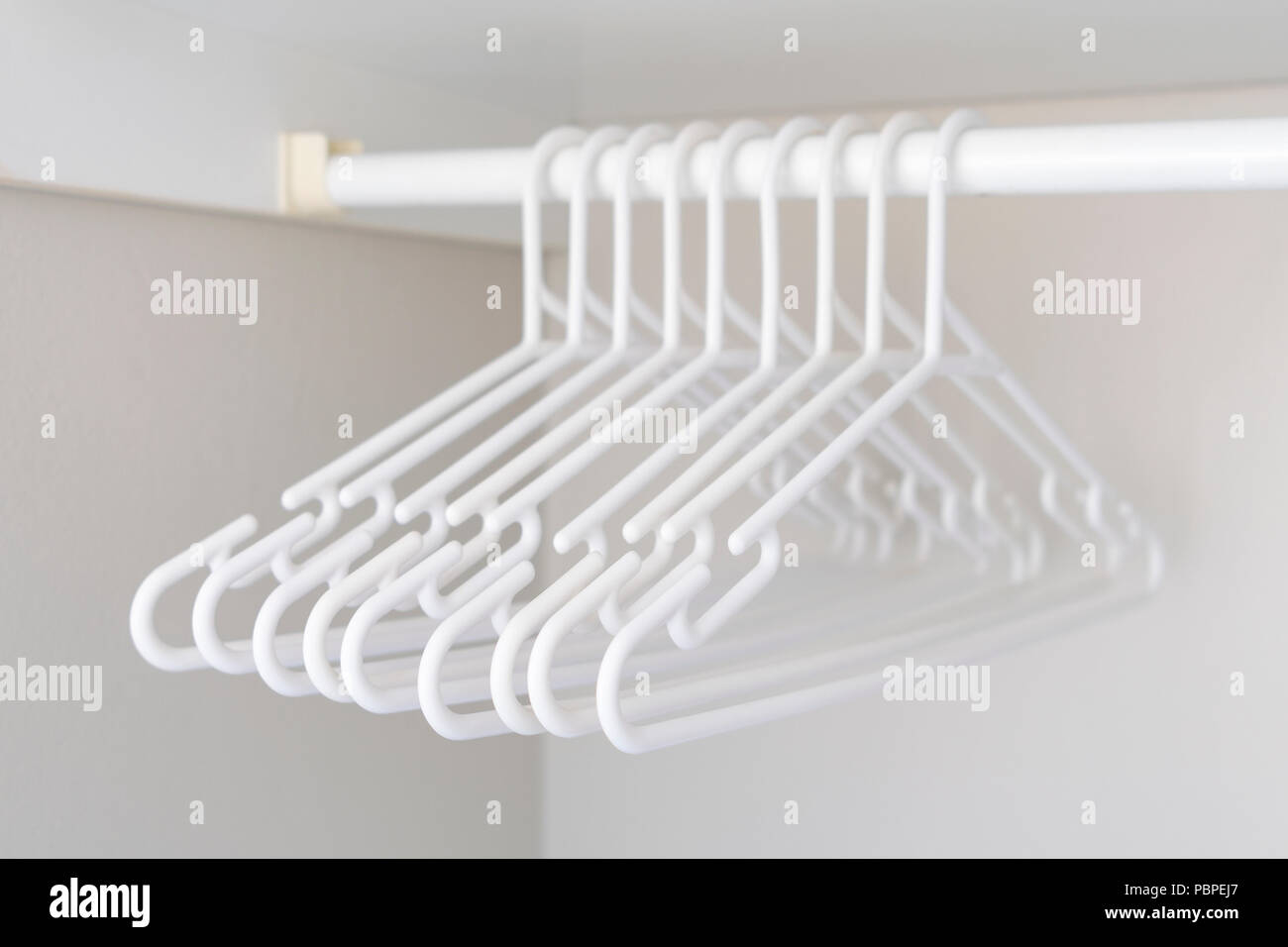 Bunch of white plastic hangers hanging on a clothes rack in the wardrobe Stock Photo
