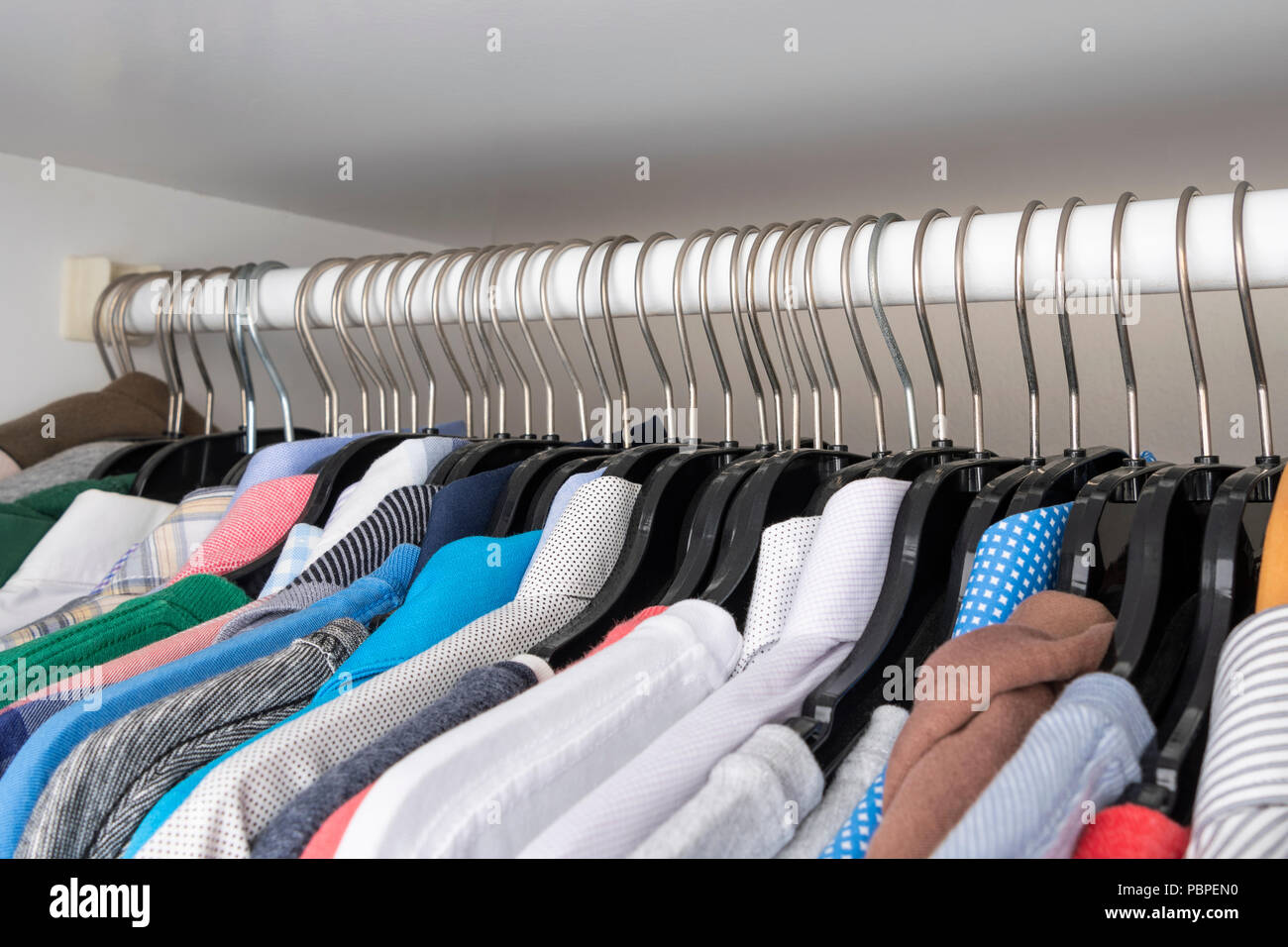 Choice of clothes of different colors hang on plastic hangers in a wardrobe Stock Photo