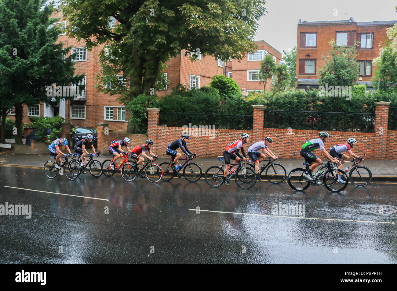 London UK. 29th July 2018. Cyclists  pass through Wimbledon village in the Prudential London Surrey 100 classic event in wet conditions as the rains start to come down. The Prudential Ride London-Surrey 100 in its 6th year celebrates  the legacy for cycling created by the London 2012 Olympic and Paralympic Games and  follows a 100-mile route on closed roads through the capital and into Surrey  countryside Credit: amer ghazzal/Alamy Live News Stock Photo