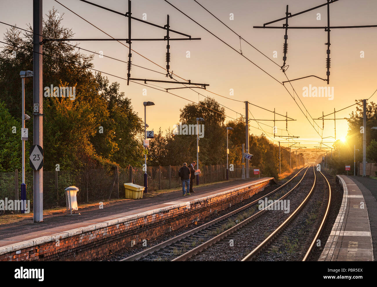 Waiting on a railway platform for a train in the early morning as the sun comes up. Bellshill Station, Glasgow, Scotland. Stock Photo