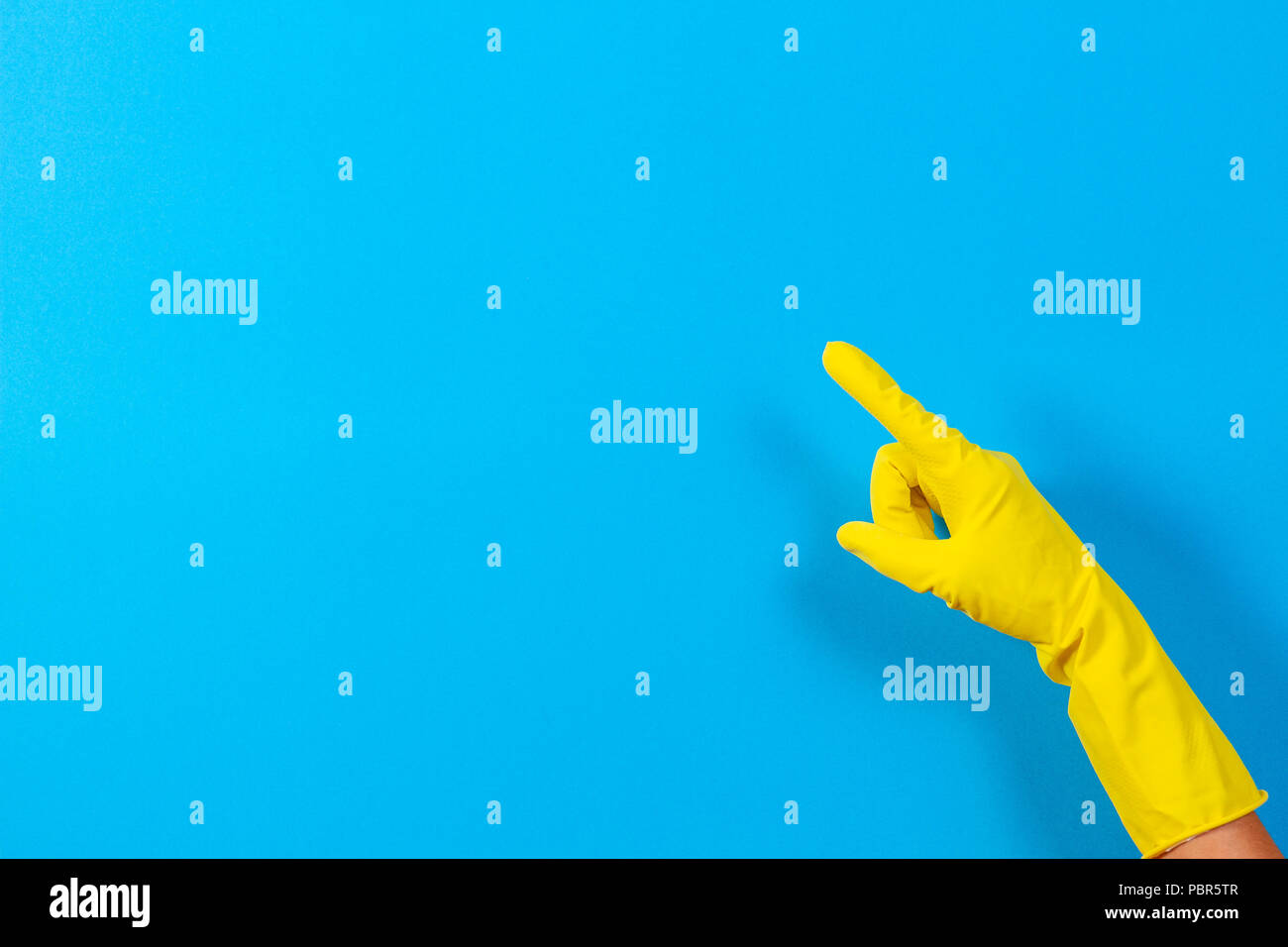 Woman hand with yellow rubber glove points upwards with index finger, blue background Stock Photo