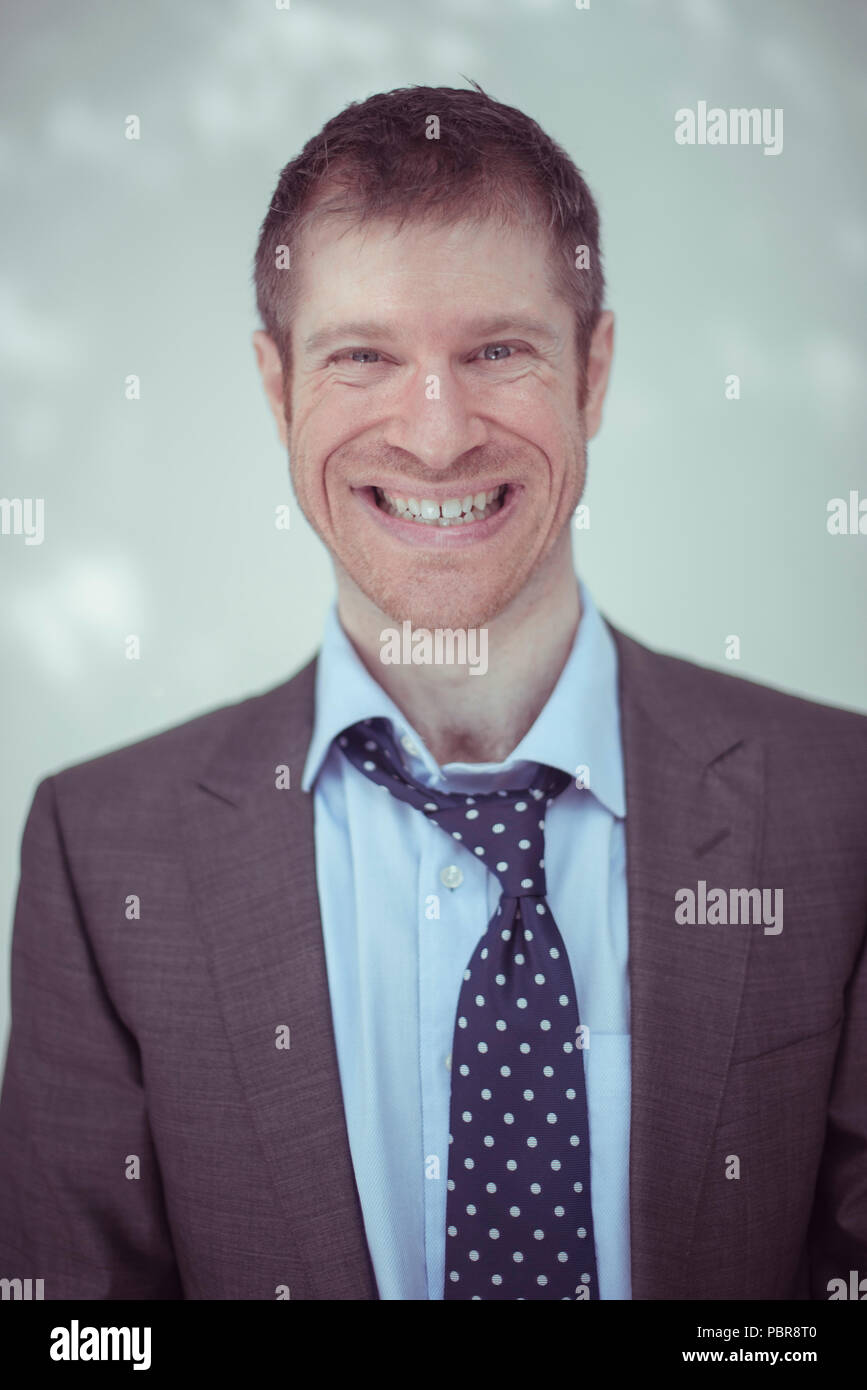 Caucasian male in his 30's wearing a grey suit, unbuttoned shirt and loosened tie, with a big fake smile. Stock Photo