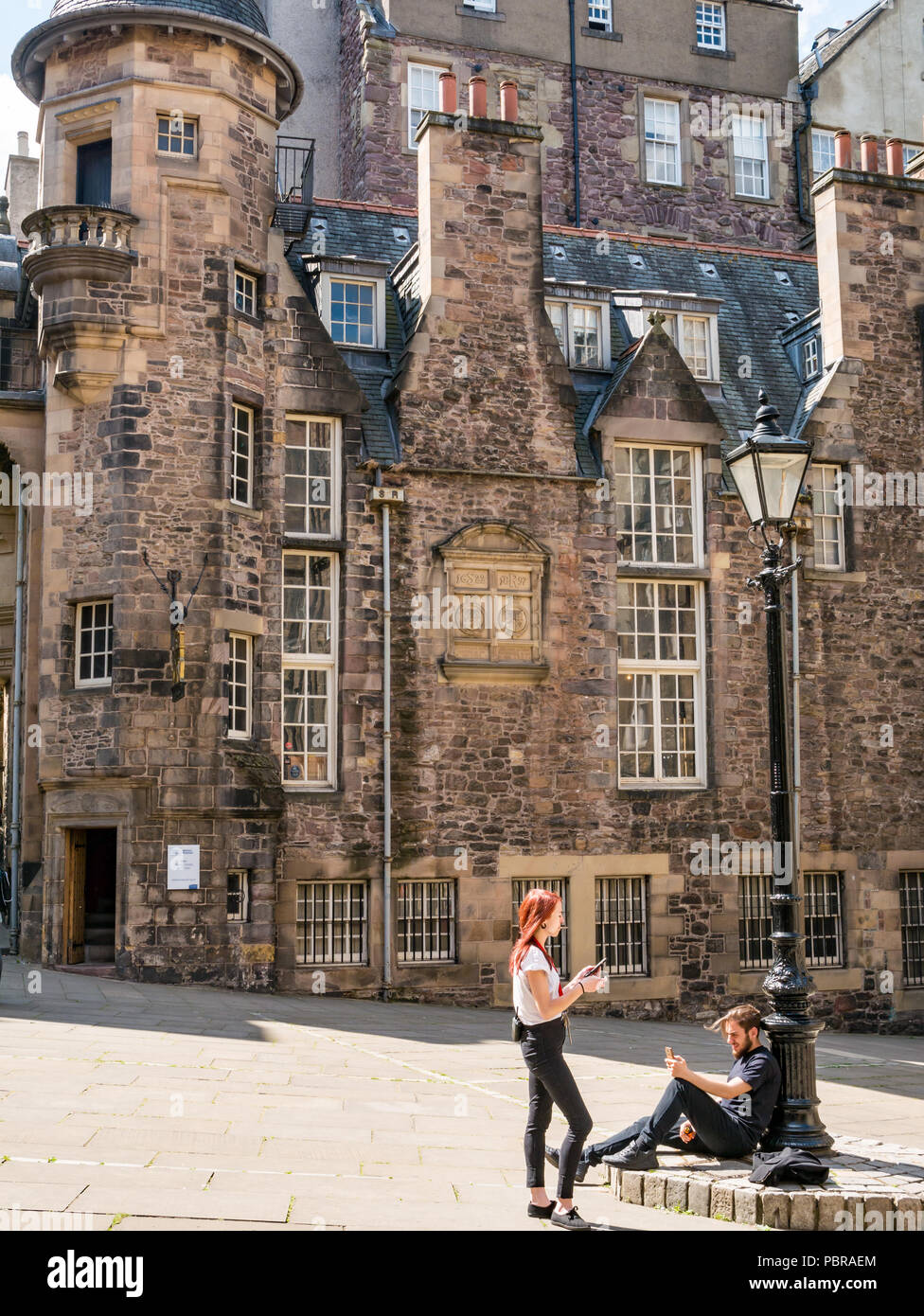 Young couple by old fashioned lamp post relax looking at phones and smoking in Makar’s Court outside Writer's Museum, Edinburgh, Scotland, UK Stock Photo