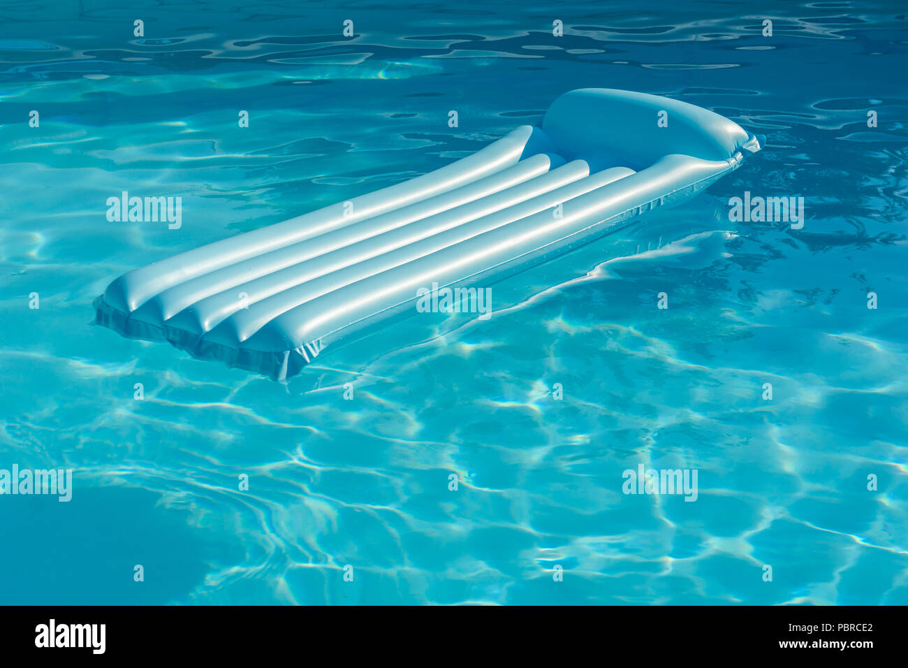 Blue inflatable mattress pool raft with sunlight floating over a swimming pool water. Summer and holidays concept. Stock Photo