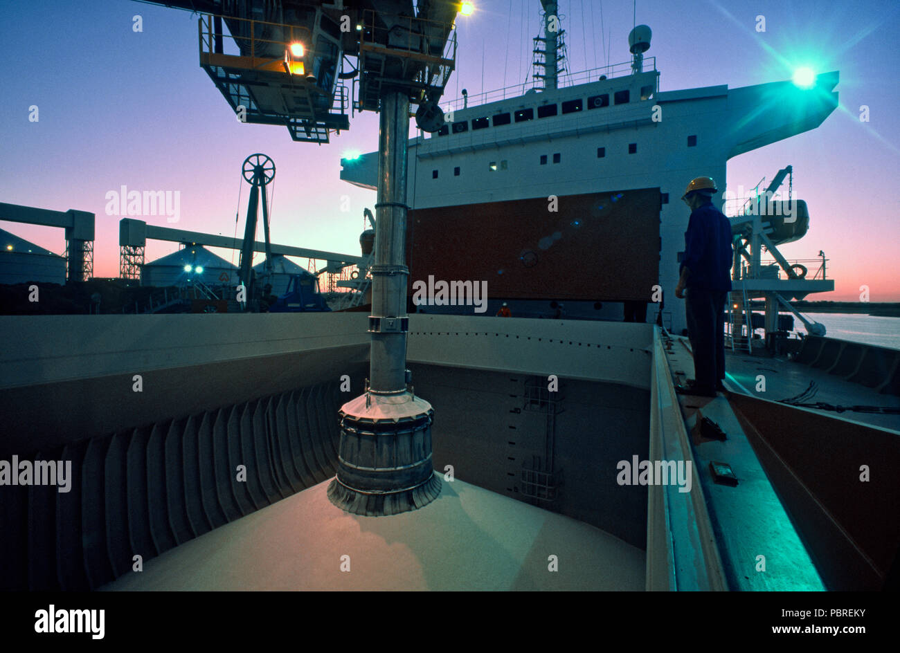 Loading alumina ore in container ship's hold at night, wide angle view Stock Photo