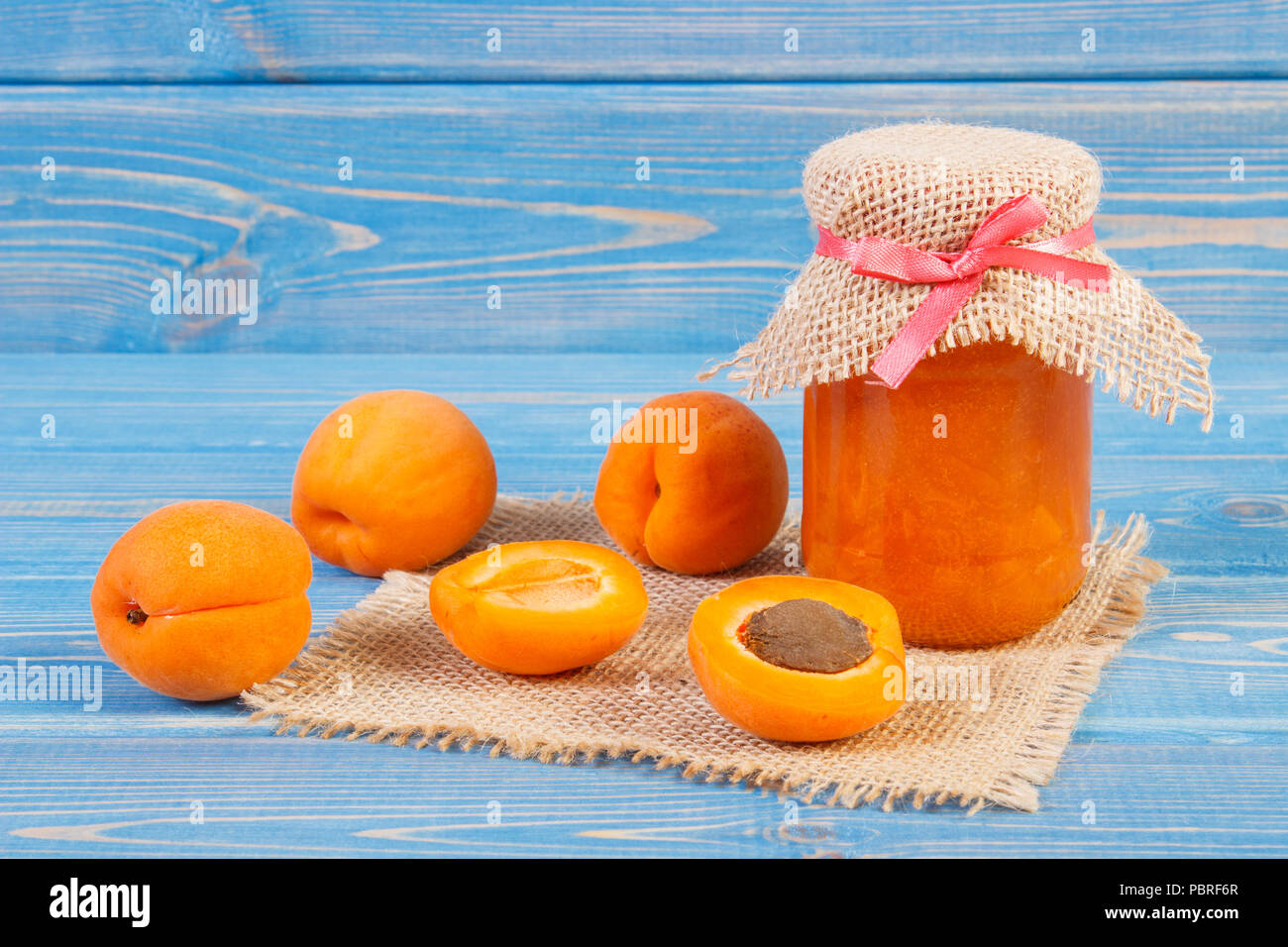 Fresh homemade apricot marmalade in jar and ripe fruits on blue boards, concept of healthy sweet dessert Stock Photo