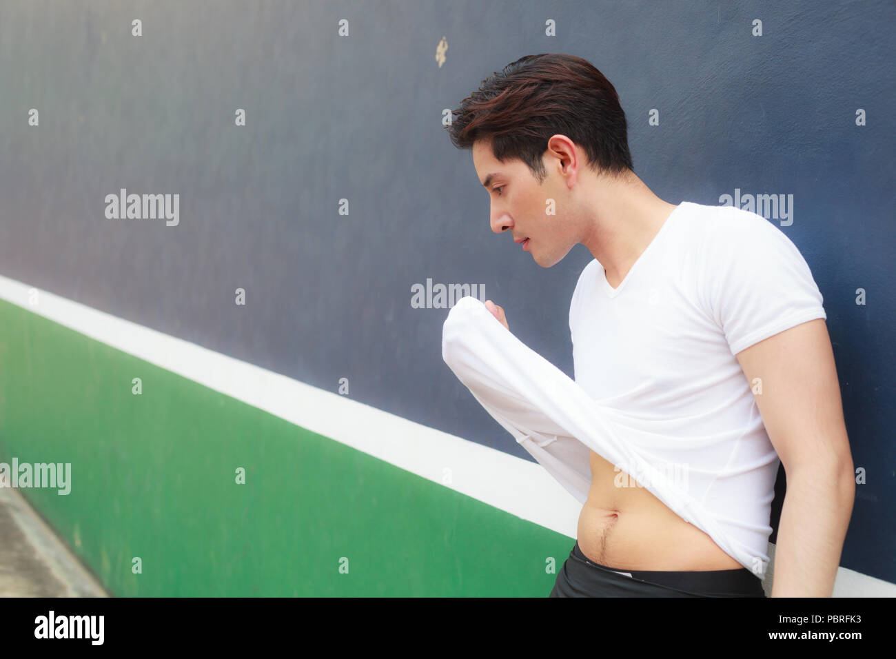 young handsome athlete man wiping sweat on his face with his white T-shirt on sport club background after exercise Stock Photo