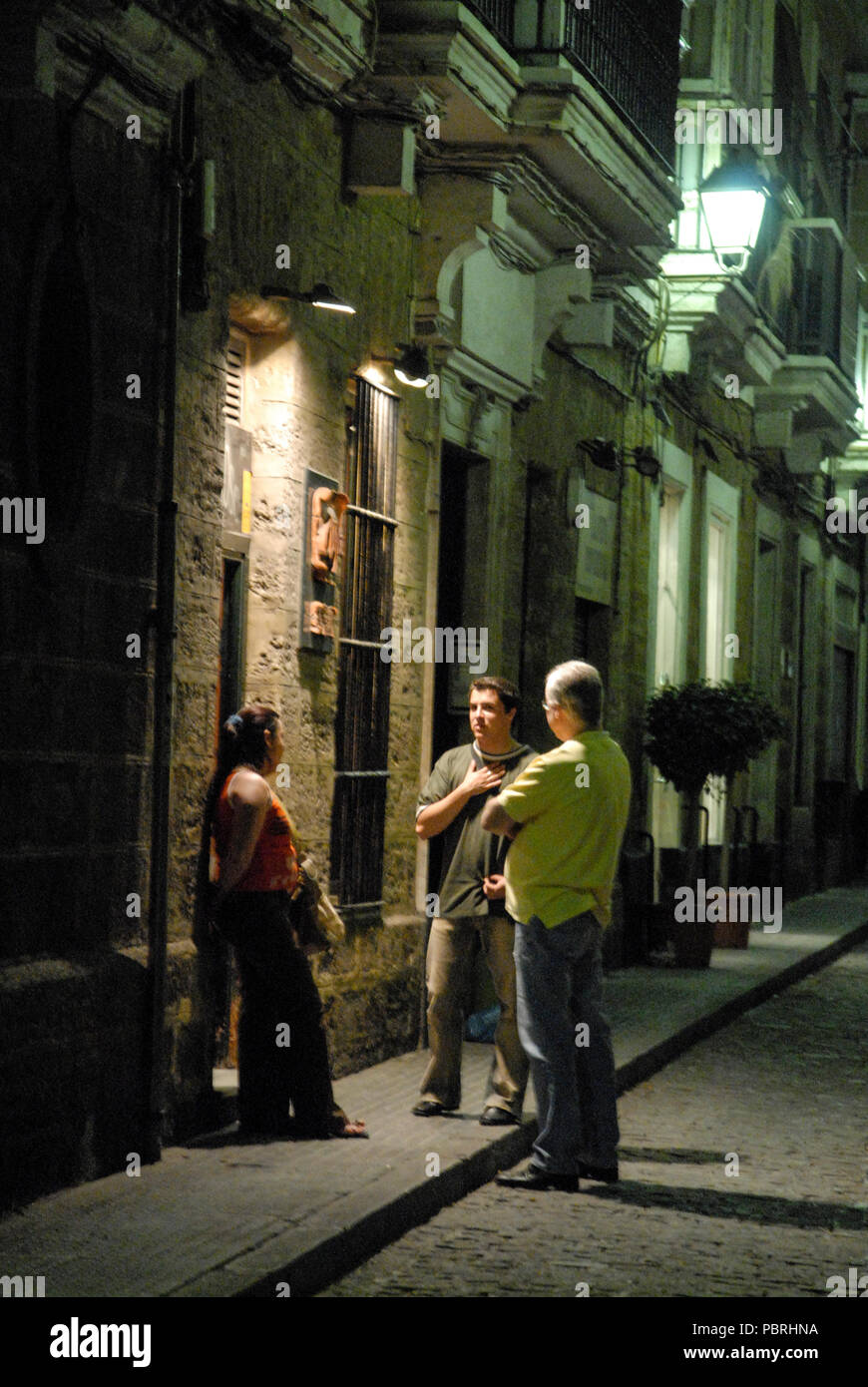 Locals standing outside a bar in one of the narrow streets in the Night life in the old town, Cadiz in Andalusia/ Cadiz-province, Southern Spain. Stock Photo